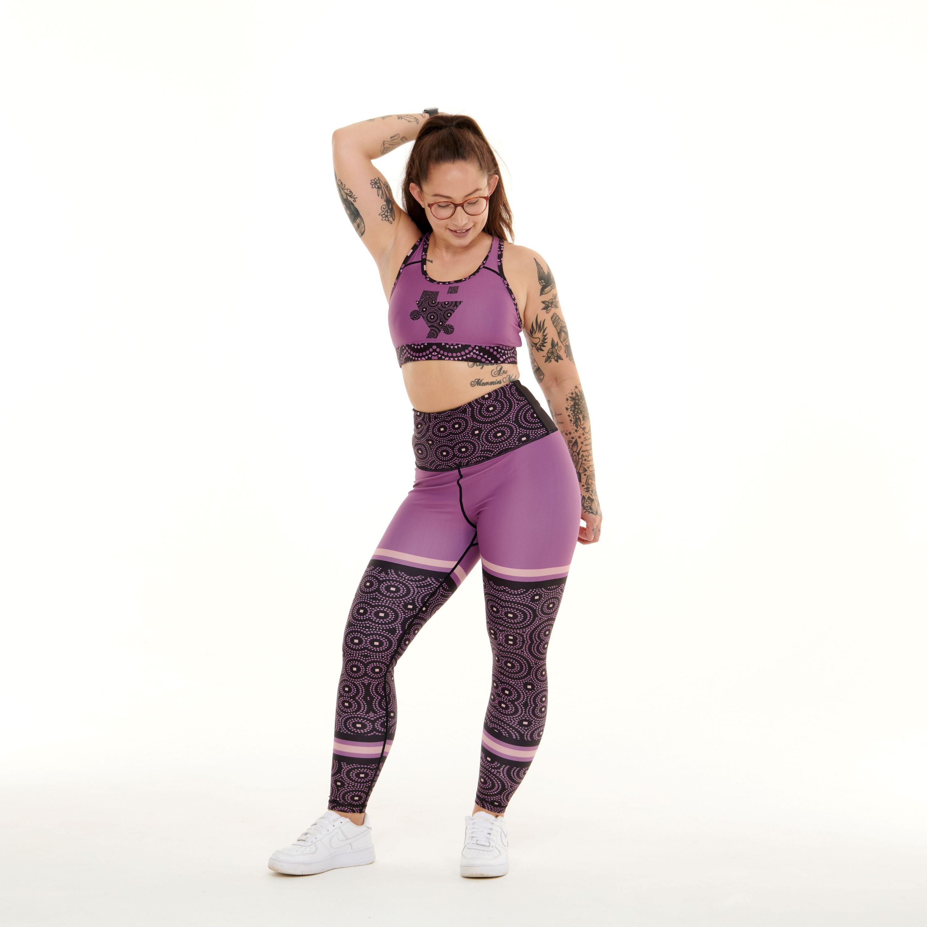 A pair of vibrant purple leggings featuring unique TYNA Signature Print with triangle, square, and circle shapes.