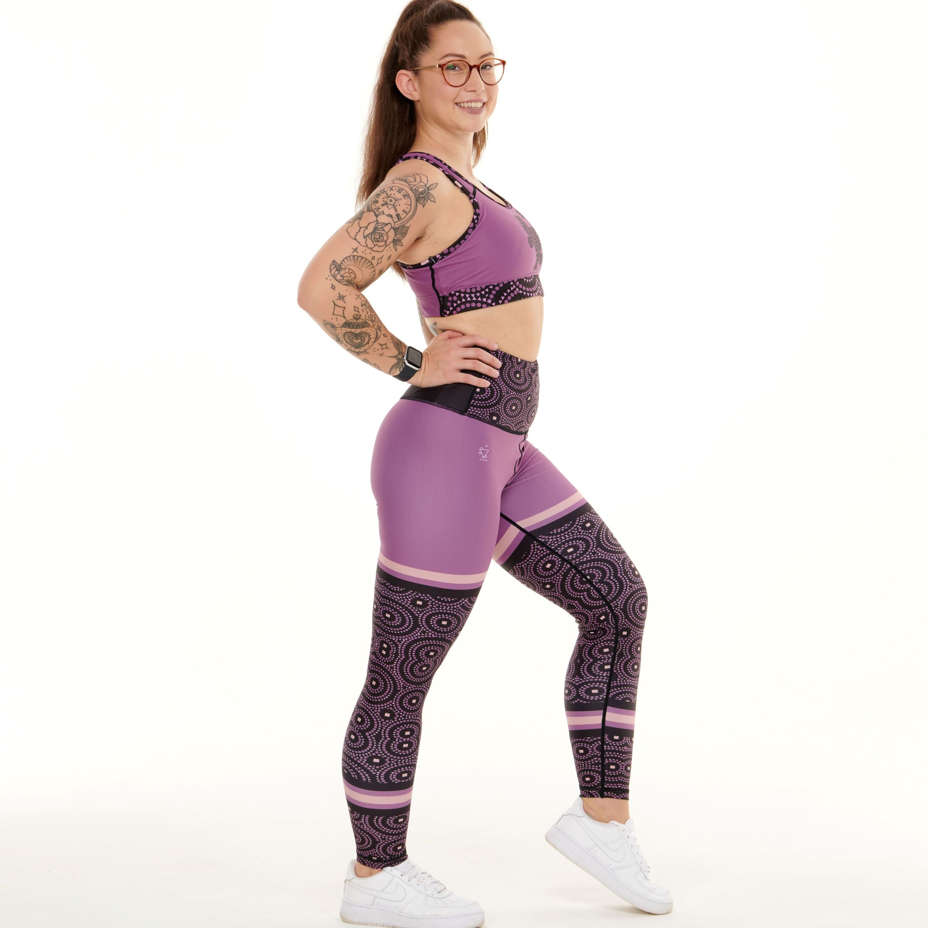 A pair of vibrant purple leggings featuring unique TYNA Signature Print with triangle, square, and circle shapes.