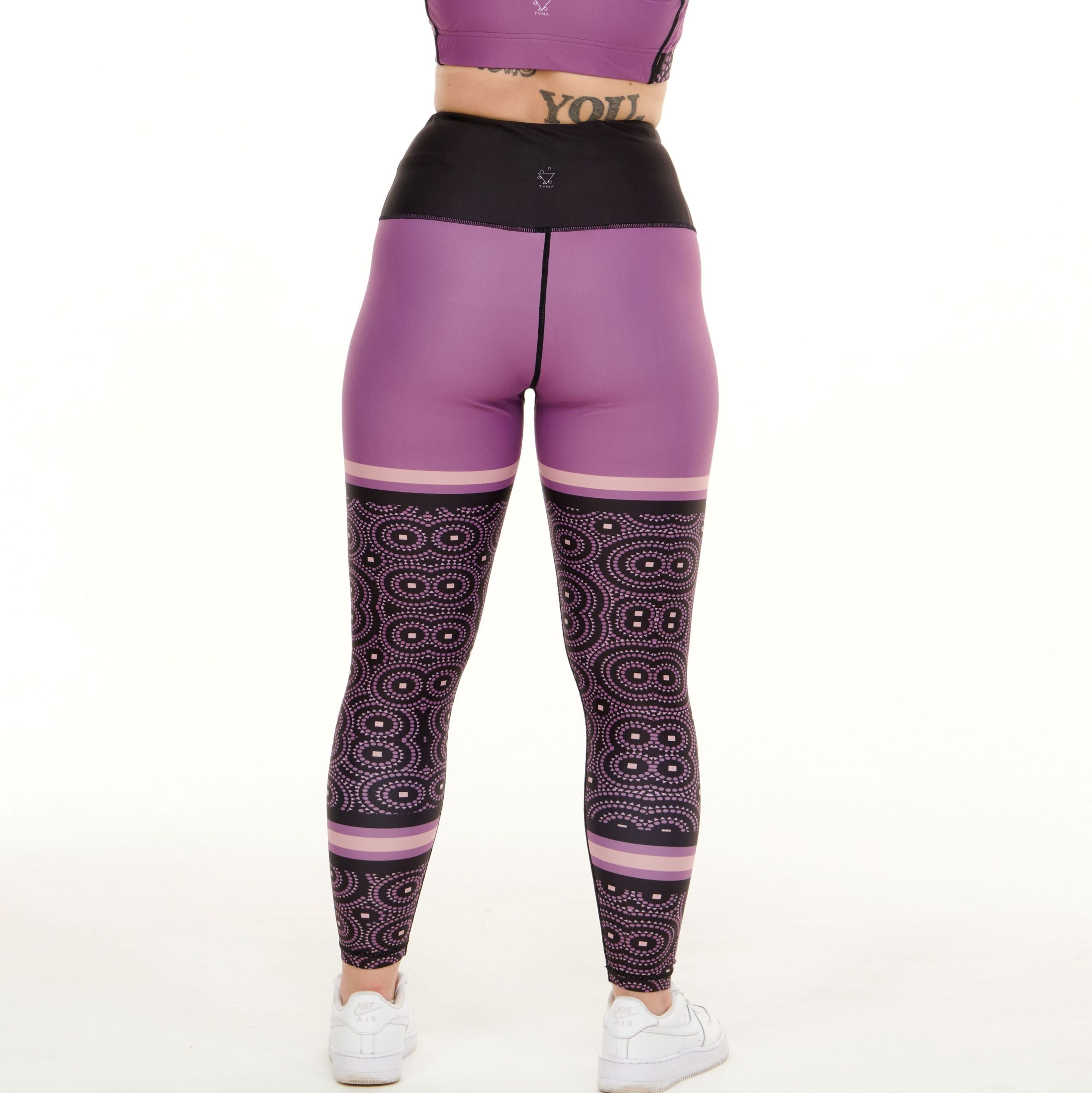 A pair of vibrant purple leggings featuring unique TYNA Signature Print with triangle, square, and circle shapes.