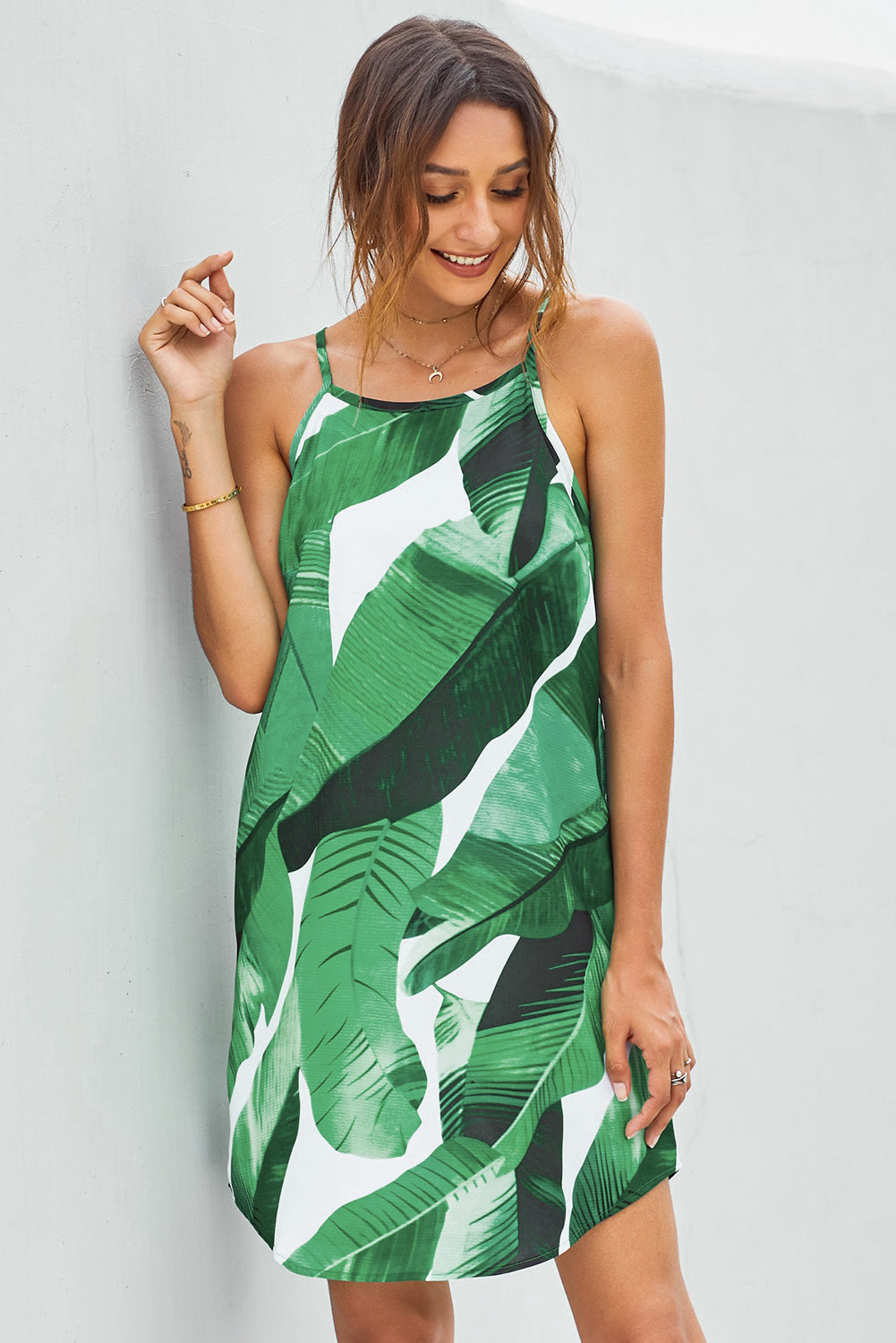 A stylish green leaf print sleeveless summer dress with a high neck and mini length, featuring a curved hemline and soft fabric, perfect for summer outings.