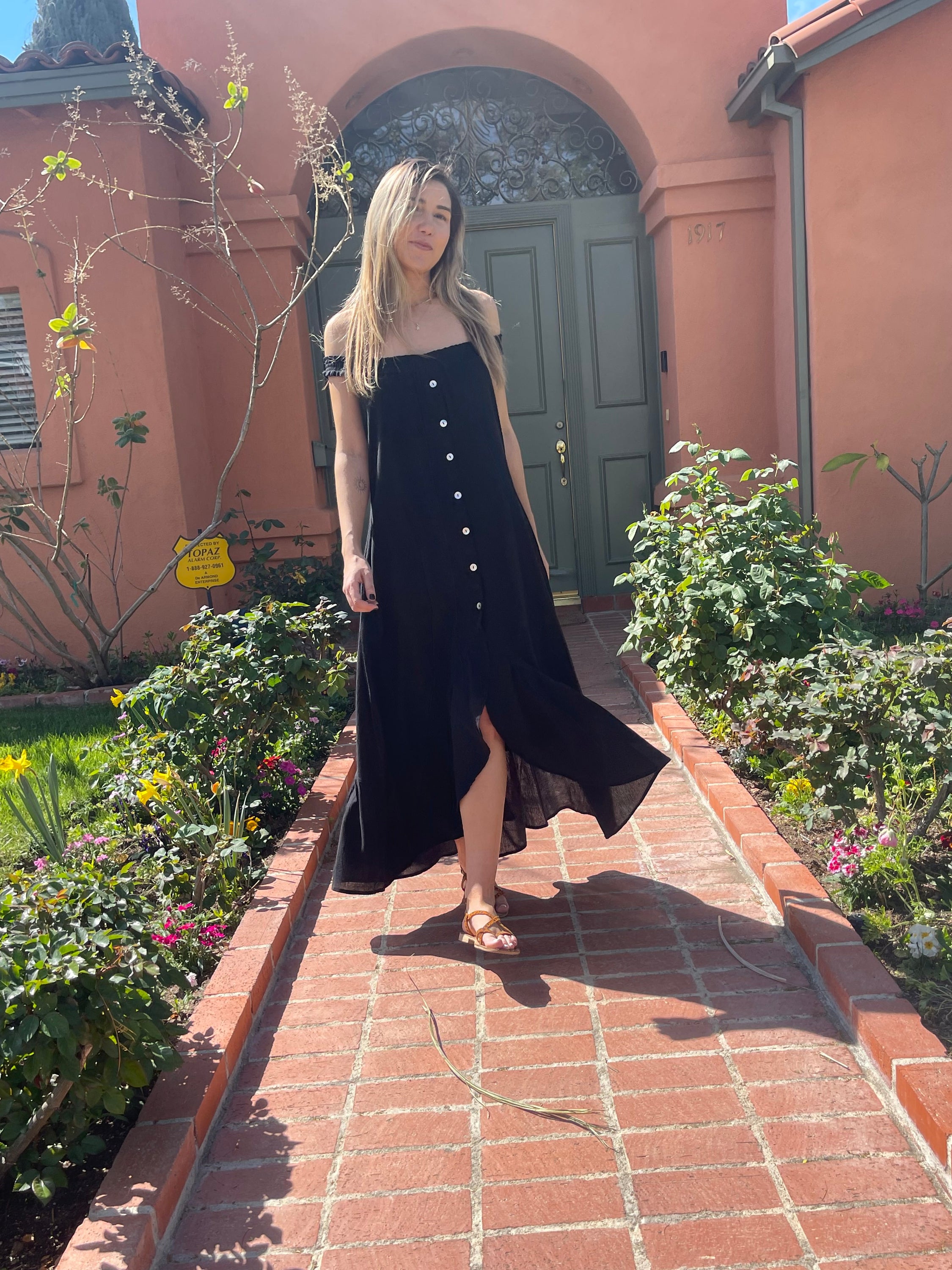 A stylish black MALIBU MAXI DRESS featuring a scooped neckline, shirred detailing, and mother-of-pearl buttons, perfect for sunny occasions.