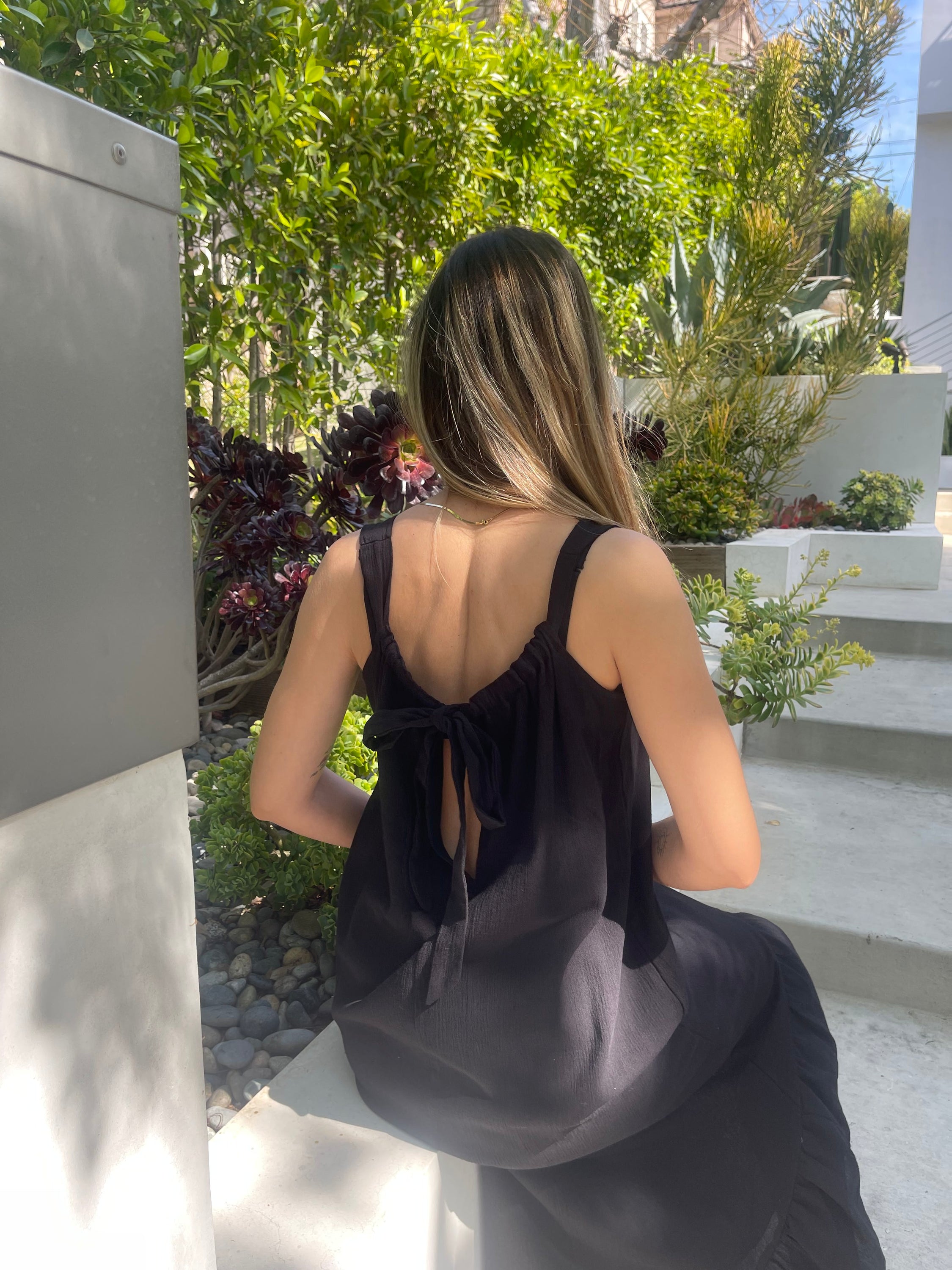 A stylish black maxi dress made from 100% Turkish cotton, featuring adjustable tie straps and a breezy silhouette, perfect for summer outings.