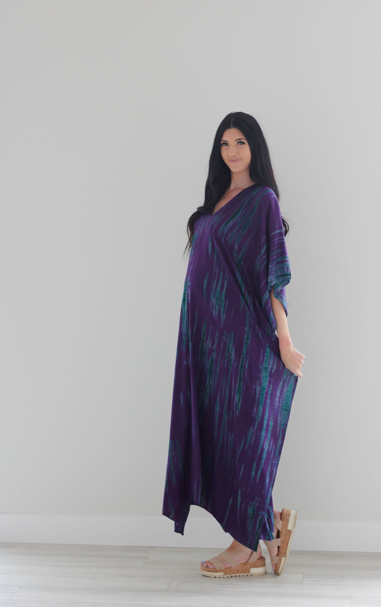 A vibrant purple tie-dyed kaftan dress with pockets, showcasing a v-shaped neck and flowing fabric, perfect for all body types.