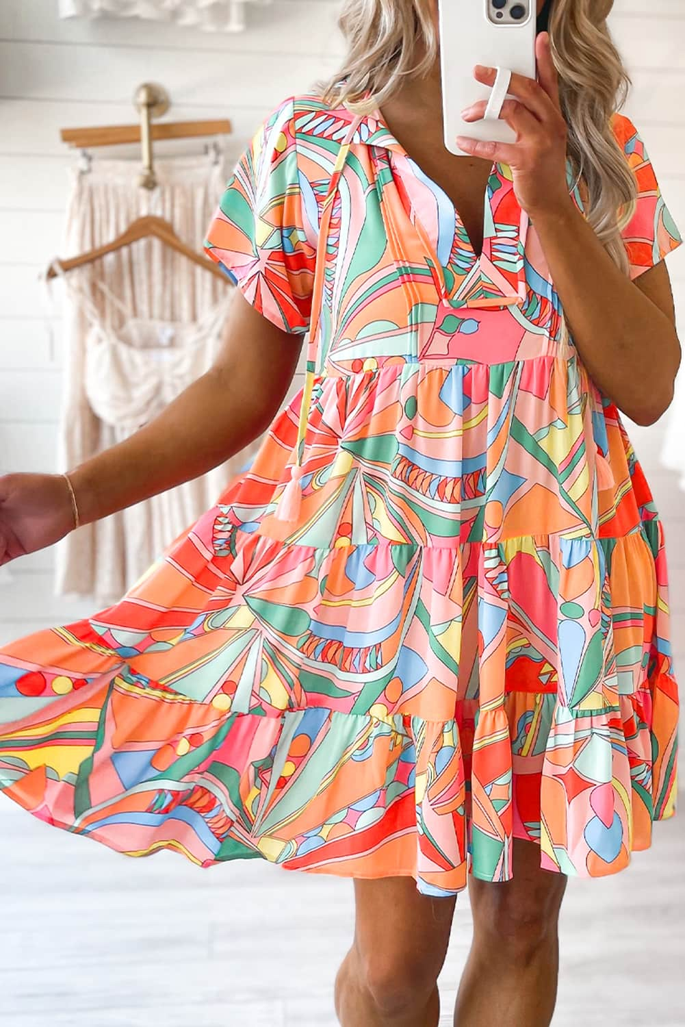 A stylish woman wearing a Tassel Tie Flared Dress with an abstract geometric print, showcasing the playful tassel tie detail.