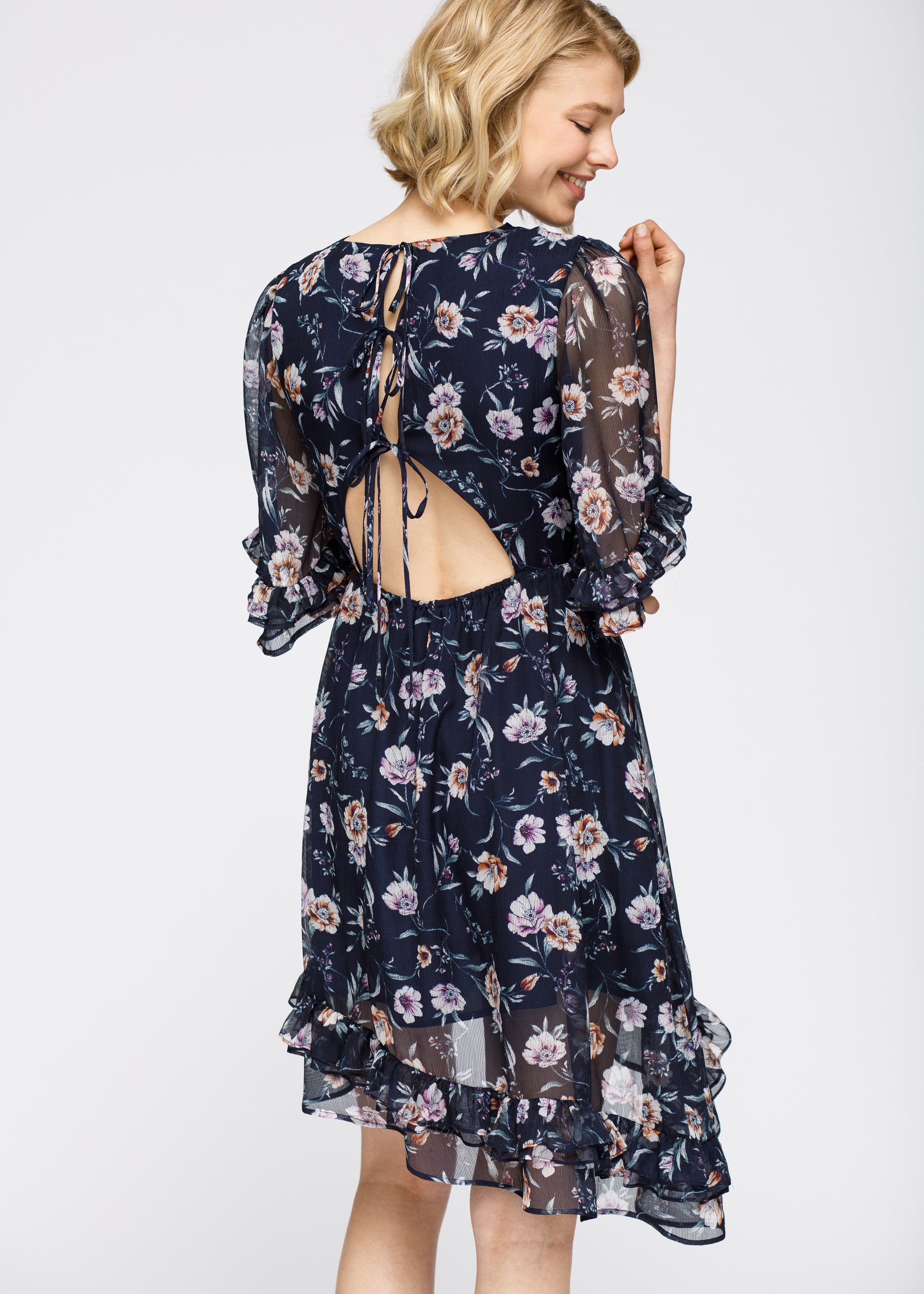 A stylish Wax Flower Asymmetrical Hi-Lo Dress featuring a sheer floral print, ruffle hem, and open back design.