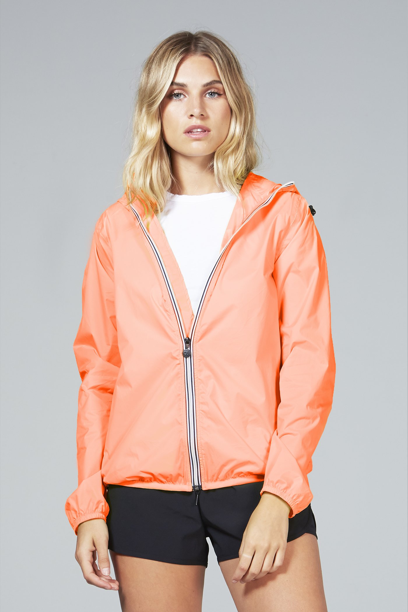 Women's orange fluo full zip packable rain jacket displayed outdoors, showcasing its vibrant color and packable design.