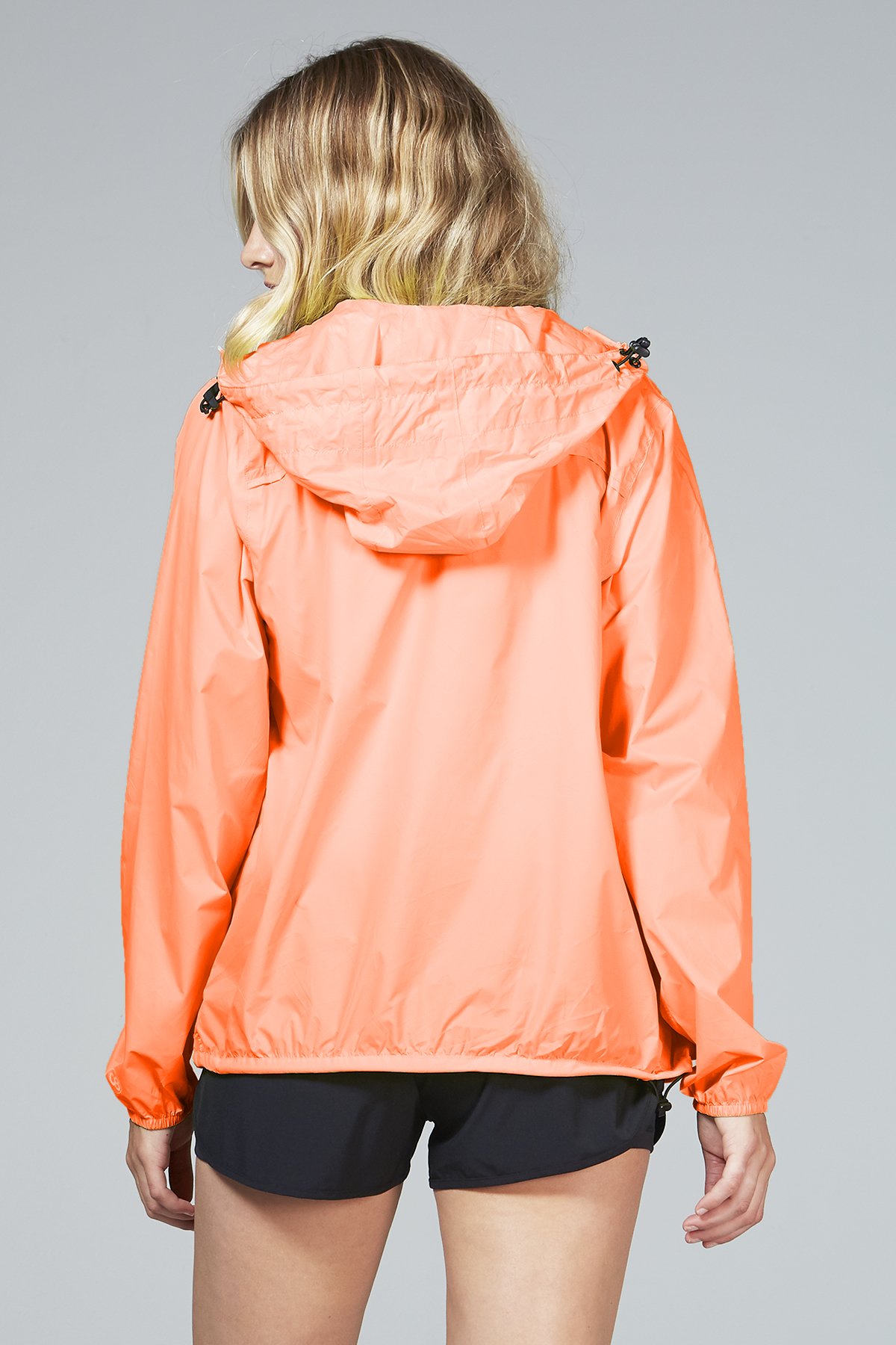 Women's orange fluo full zip packable rain jacket displayed outdoors, showcasing its vibrant color and packable design.