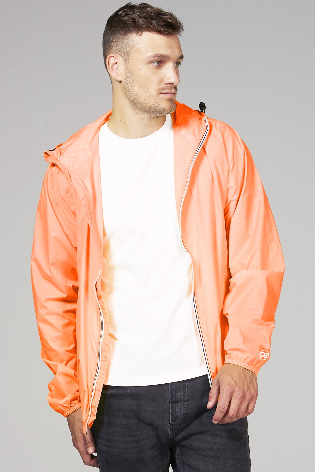 Women's orange fluo full zip packable rain jacket displayed outdoors, showcasing its vibrant color and packable design.