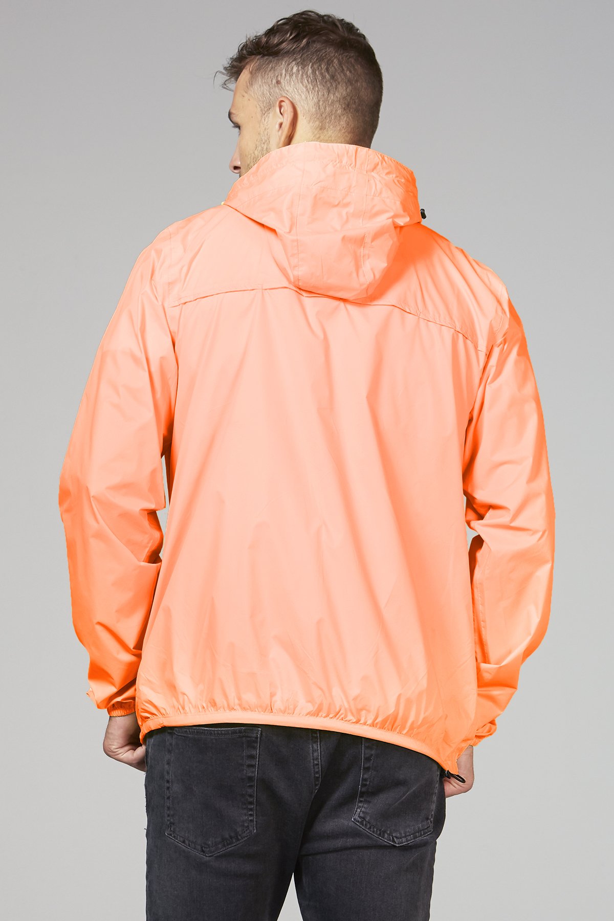 Women's orange fluo full zip packable rain jacket displayed outdoors, showcasing its vibrant color and packable design.