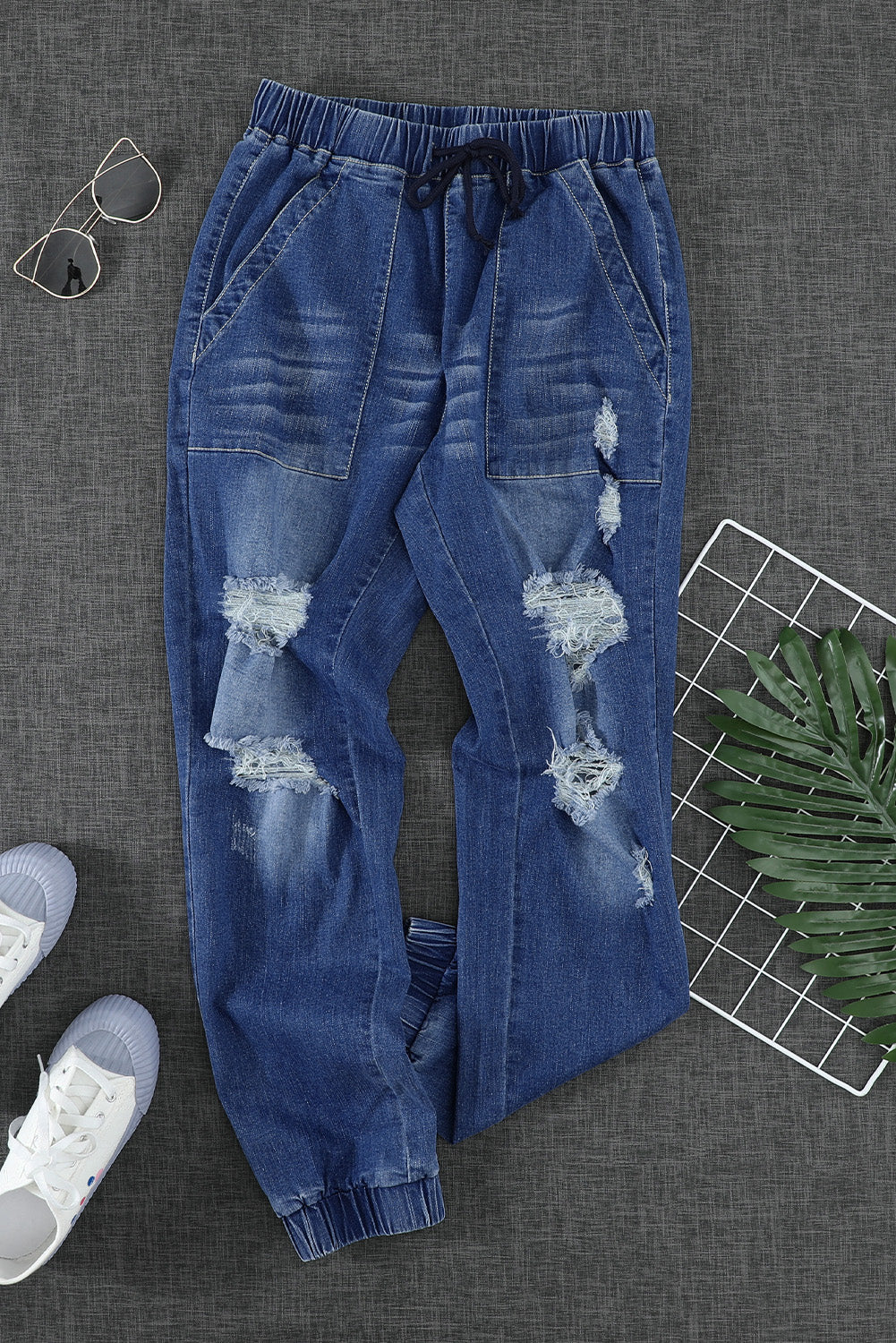 A pair of women's blue pocketed distressed denim joggers featuring an elastic waistband, tapered leg, and stylish ripped details, perfect for casual wear.