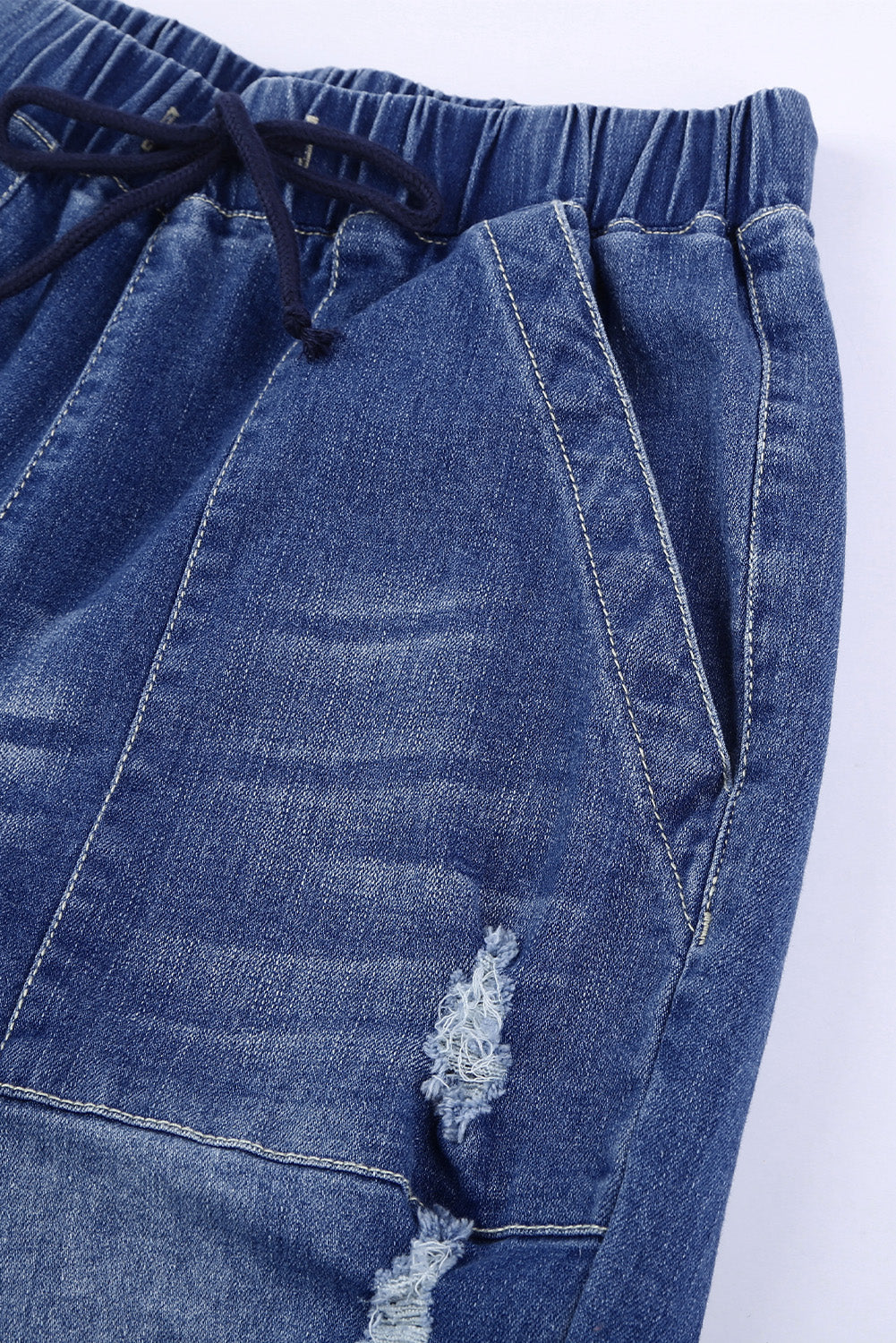 A pair of women's blue pocketed distressed denim joggers featuring an elastic waistband, tapered leg, and stylish ripped details, perfect for casual wear.