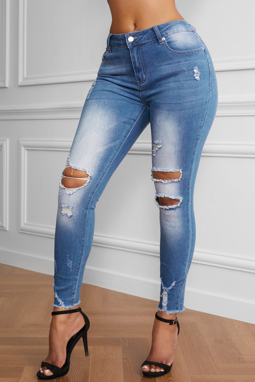 A pair of Women's Faded Mid High Rise Holes Skinny Jeans featuring distressed legs, frayed ankles, and a light blue color, styled on a mannequin.