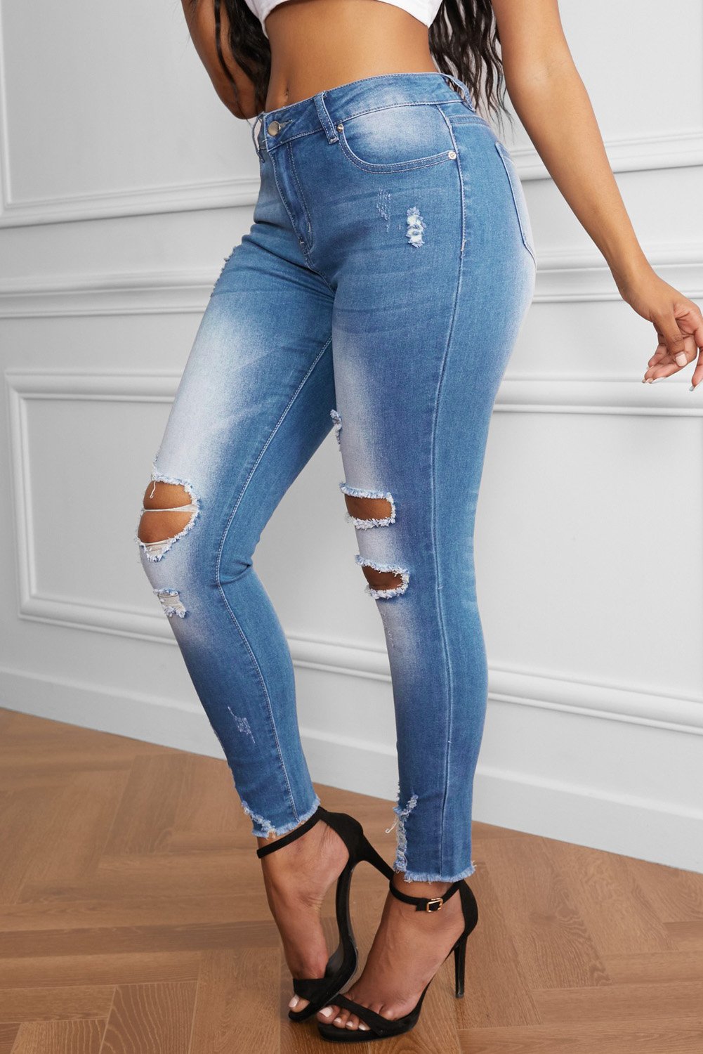 A pair of Women's Faded Mid High Rise Holes Skinny Jeans featuring distressed legs, frayed ankles, and a light blue color, styled on a mannequin.