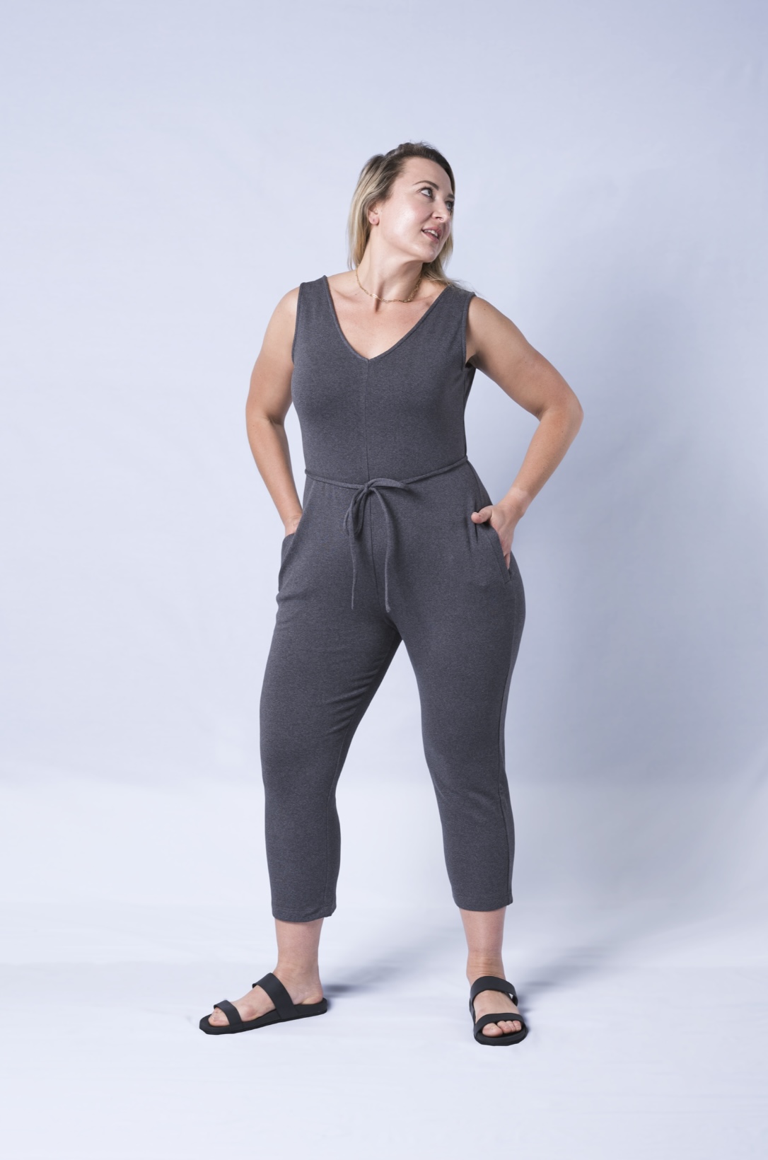 A stylish Axty V-Neck Jumpsuit featuring a self-tie waistband, deep side pockets, and a tapered mid-calf crop leg, made from soft cotton fabric.