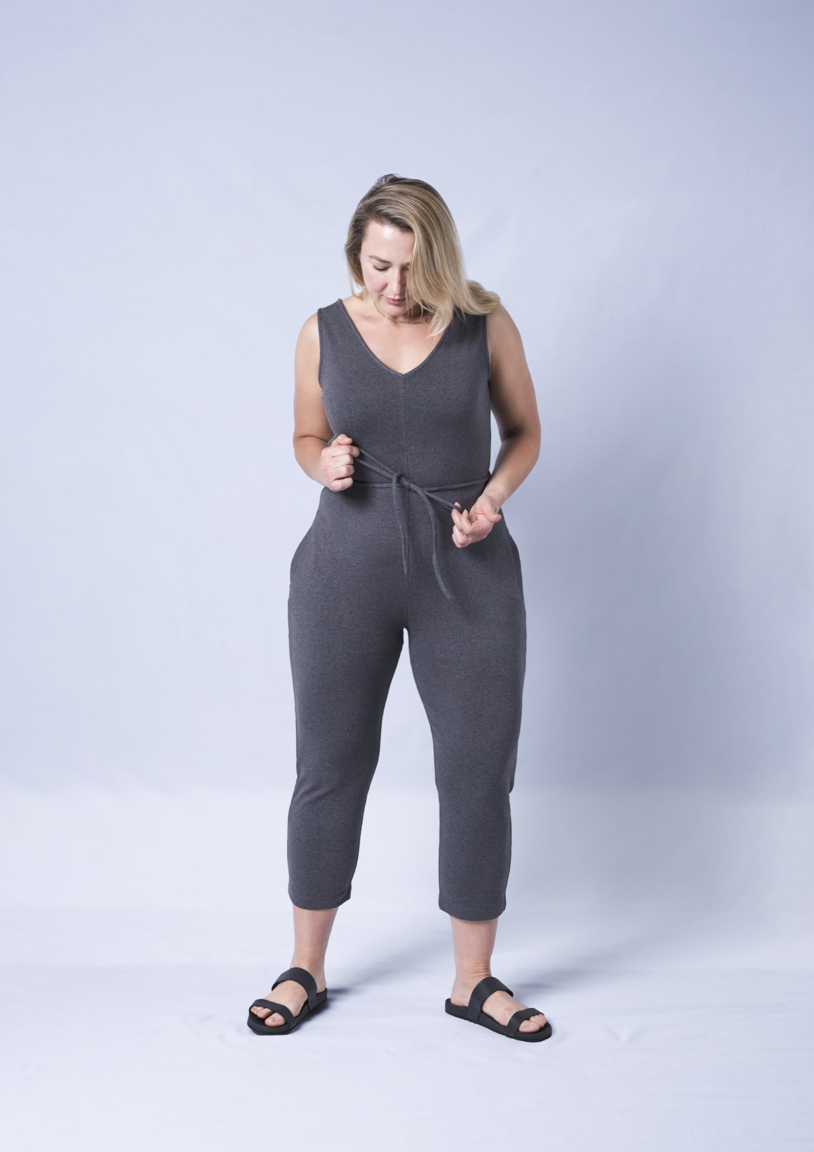 A stylish Axty V-Neck Jumpsuit featuring a self-tie waistband, deep side pockets, and a tapered mid-calf crop leg, made from soft cotton fabric.