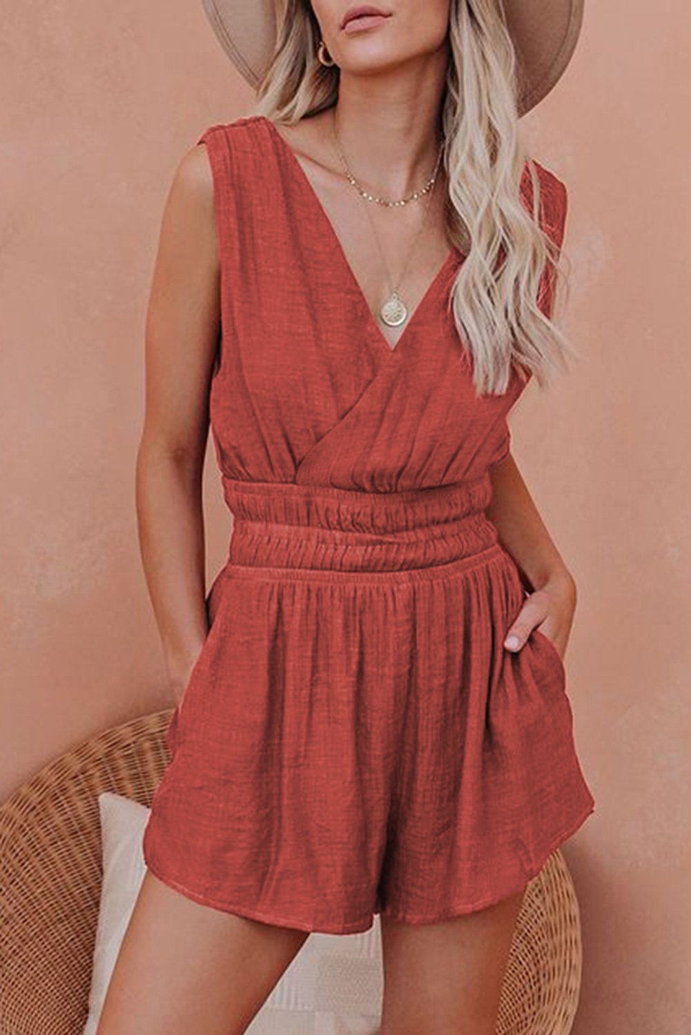 A stylish red smocked pocketed sleeveless v-neck romper, featuring a draped neckline and high-waisted shorts, perfect for summer outings.