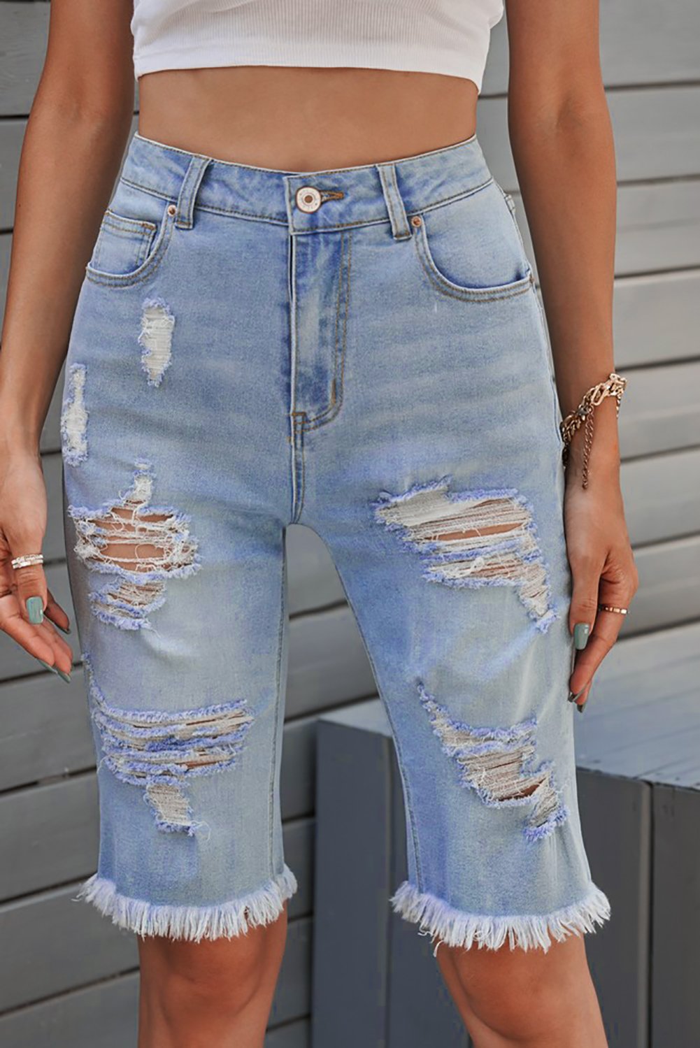 A pair of women's light blue distressed jeans Bermuda shorts featuring a raw hem, pockets, and a casual style, perfect for summer wear.