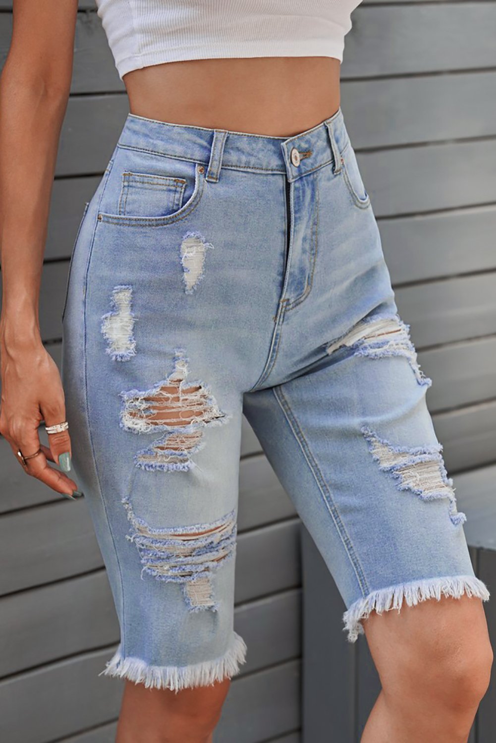 A pair of women's light blue distressed jeans Bermuda shorts featuring a raw hem, pockets, and a casual style, perfect for summer wear.