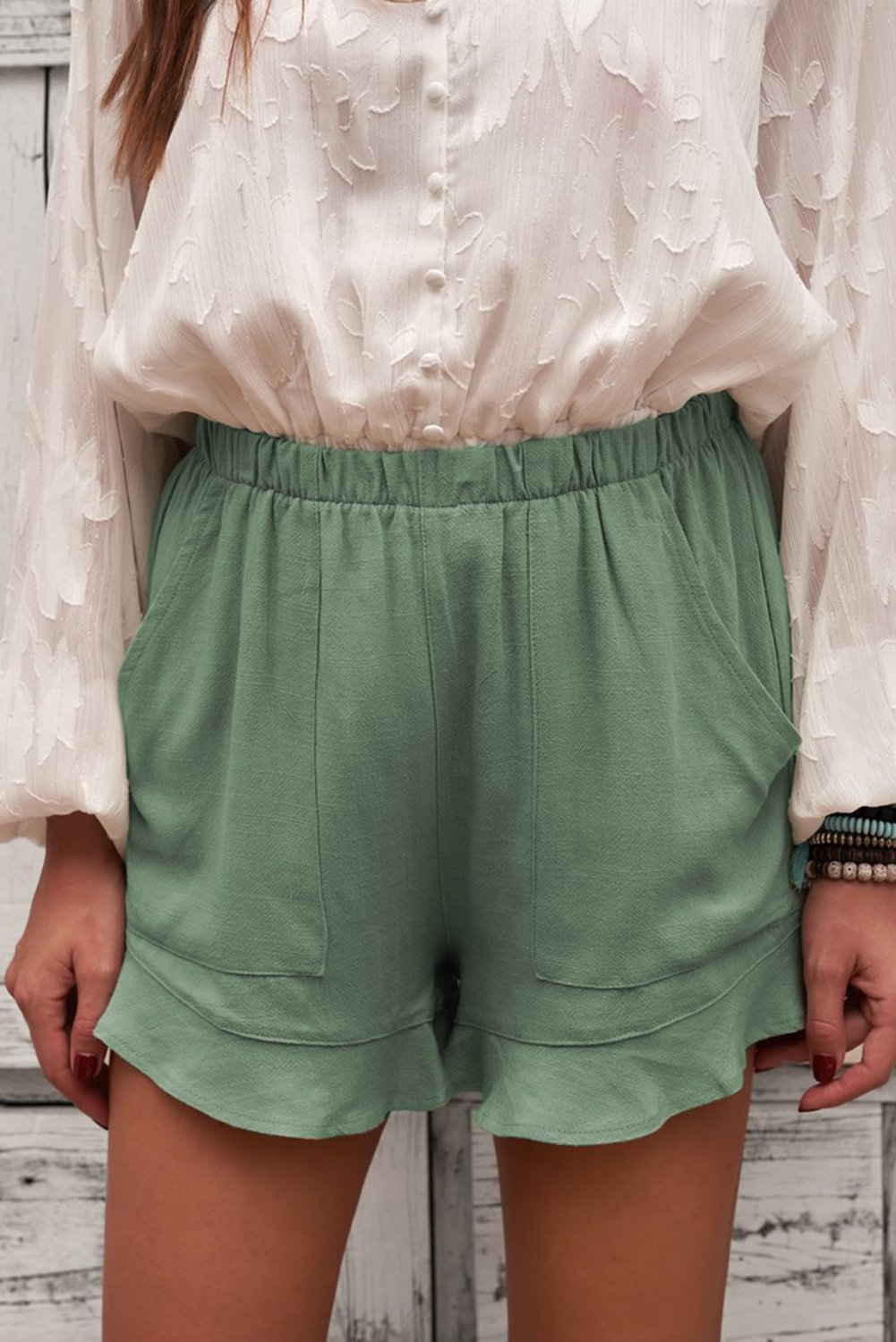 A pair of Women's Summer Pocketed Flutter Green Linen Cotton Shorts featuring ruffled details and side pockets, perfect for summer wear.