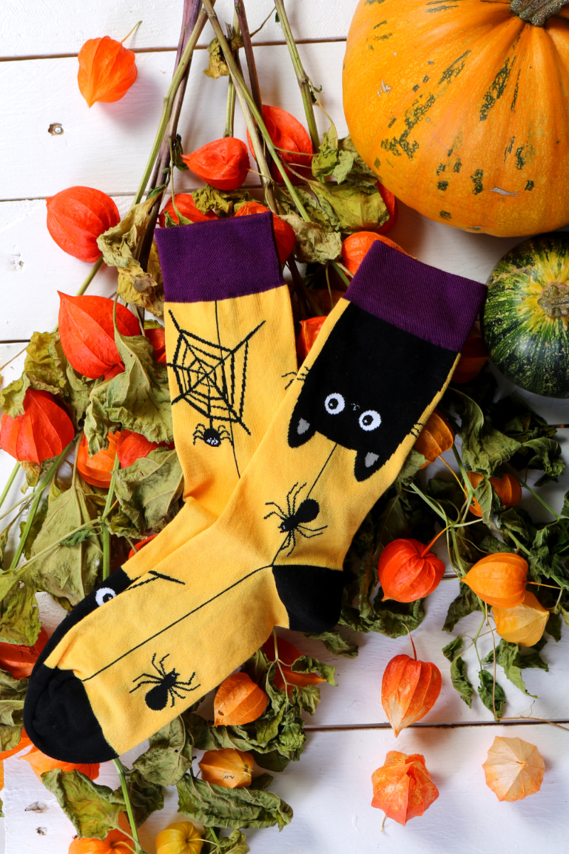 A pair of Halloween socks featuring a playful black cat design and a spider, set against a vibrant yellow background.