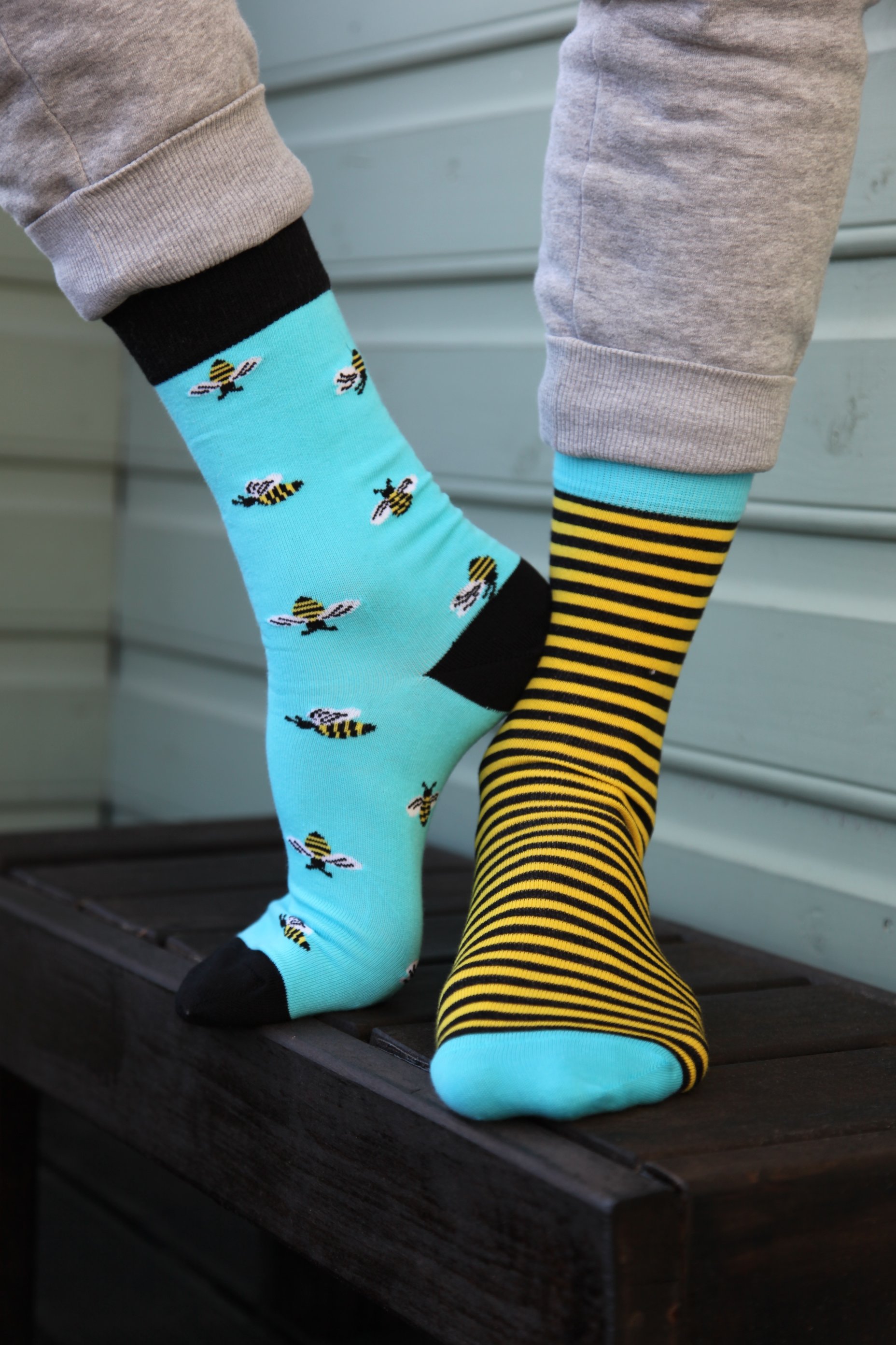 A pair of BUG men's cotton socks featuring one striped sock and one with bees, in vibrant blue and yellow colors.