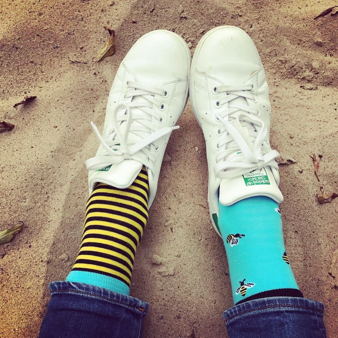 A pair of BUG men's cotton socks featuring one striped sock and one with bees, in vibrant blue and yellow colors.