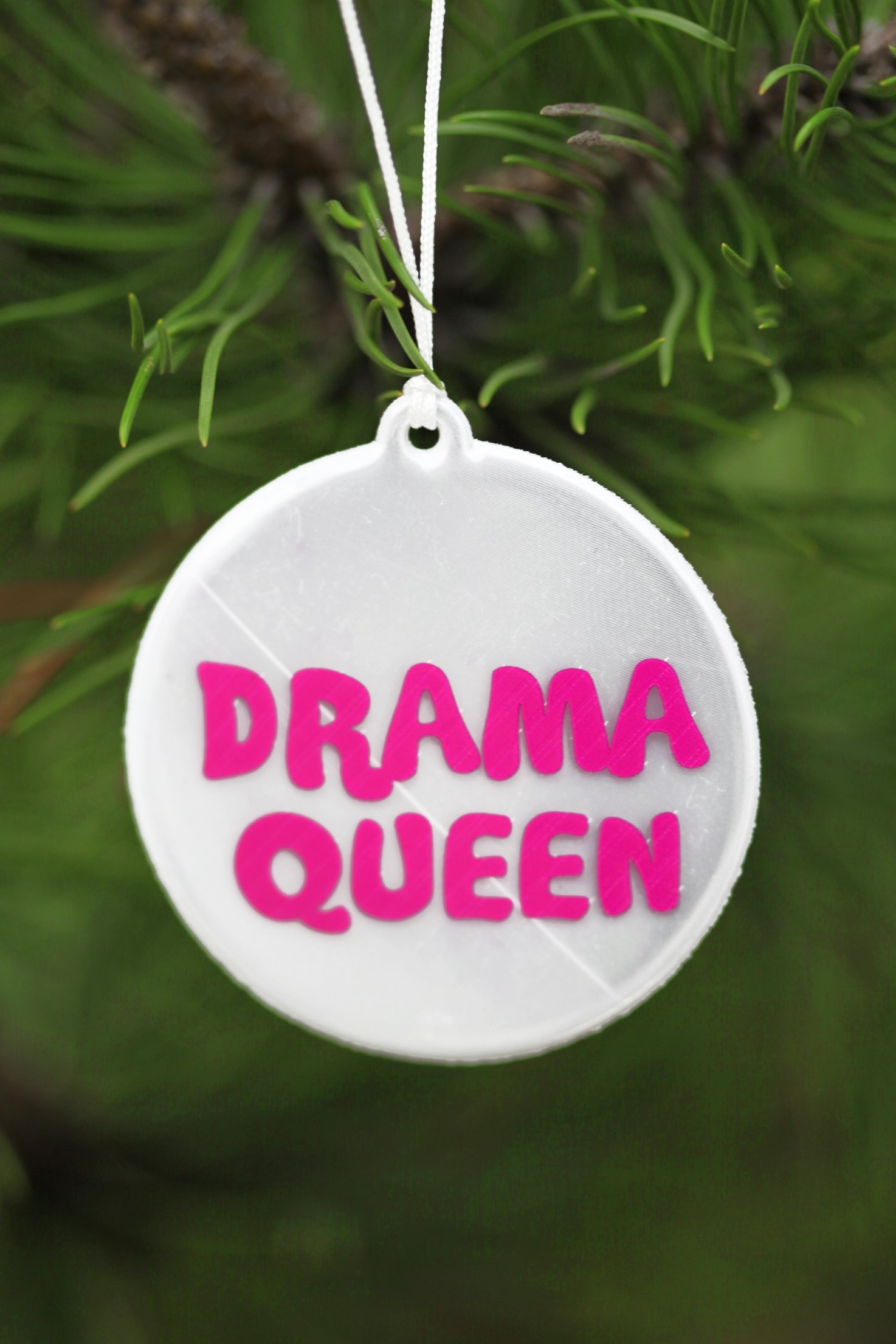 A round reflector with pink 'DRAMA QUEEN' text, measuring 60mm in diameter, attached to a 33cm string.