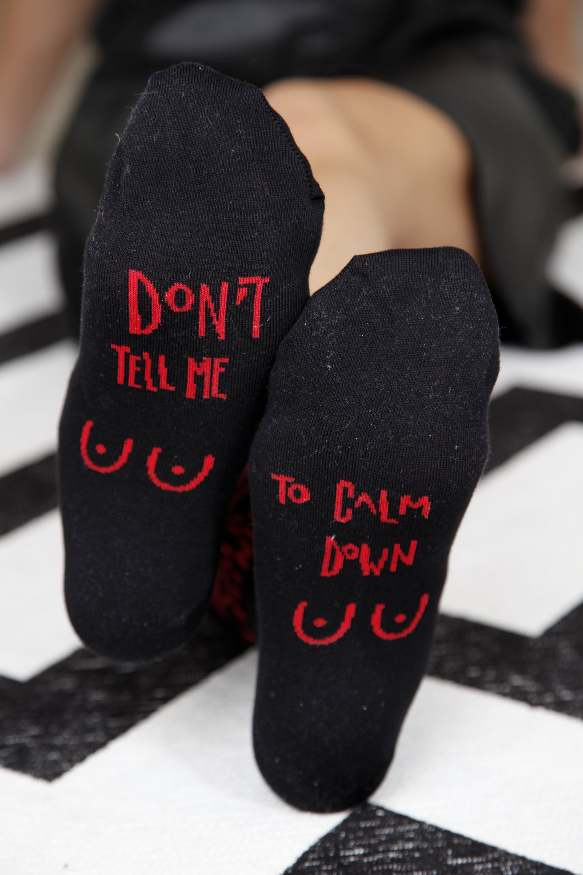 A pair of black cotton socks for women featuring the text 'WILD FEMINIST' on the side and 'Don't tell me to calm down' on the sole.