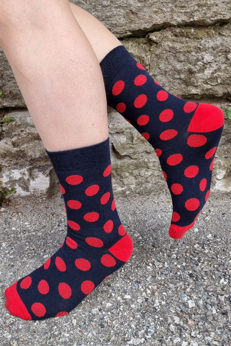 A pair of dark blue socks with red dots, made from recycled cotton, showcasing a stylish and eco-friendly design.