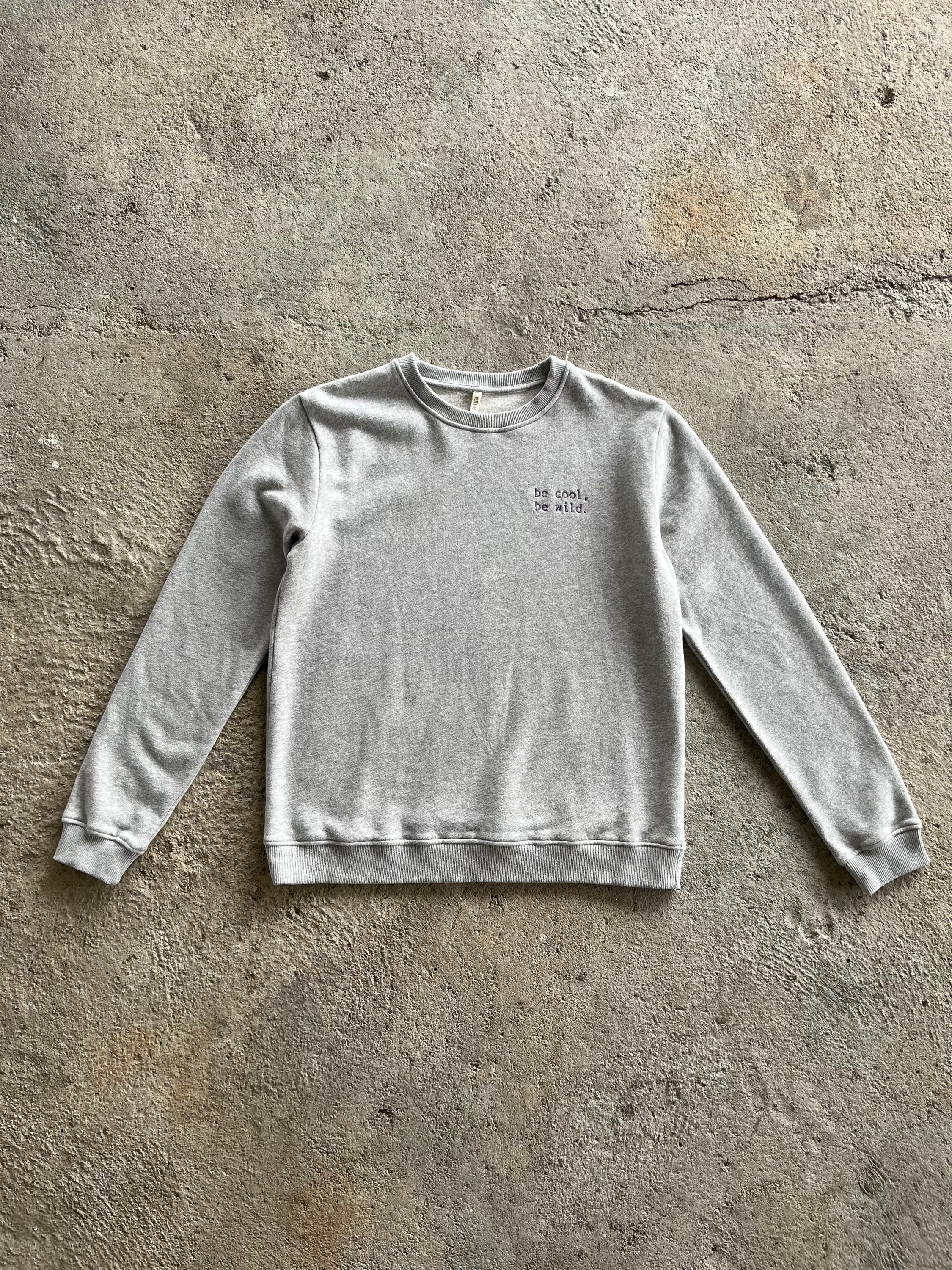 A stylish Bass Grey sweatshirt for women featuring ribbed cuffs, neckline, and a playful side print that says 'be cool, be wild'.