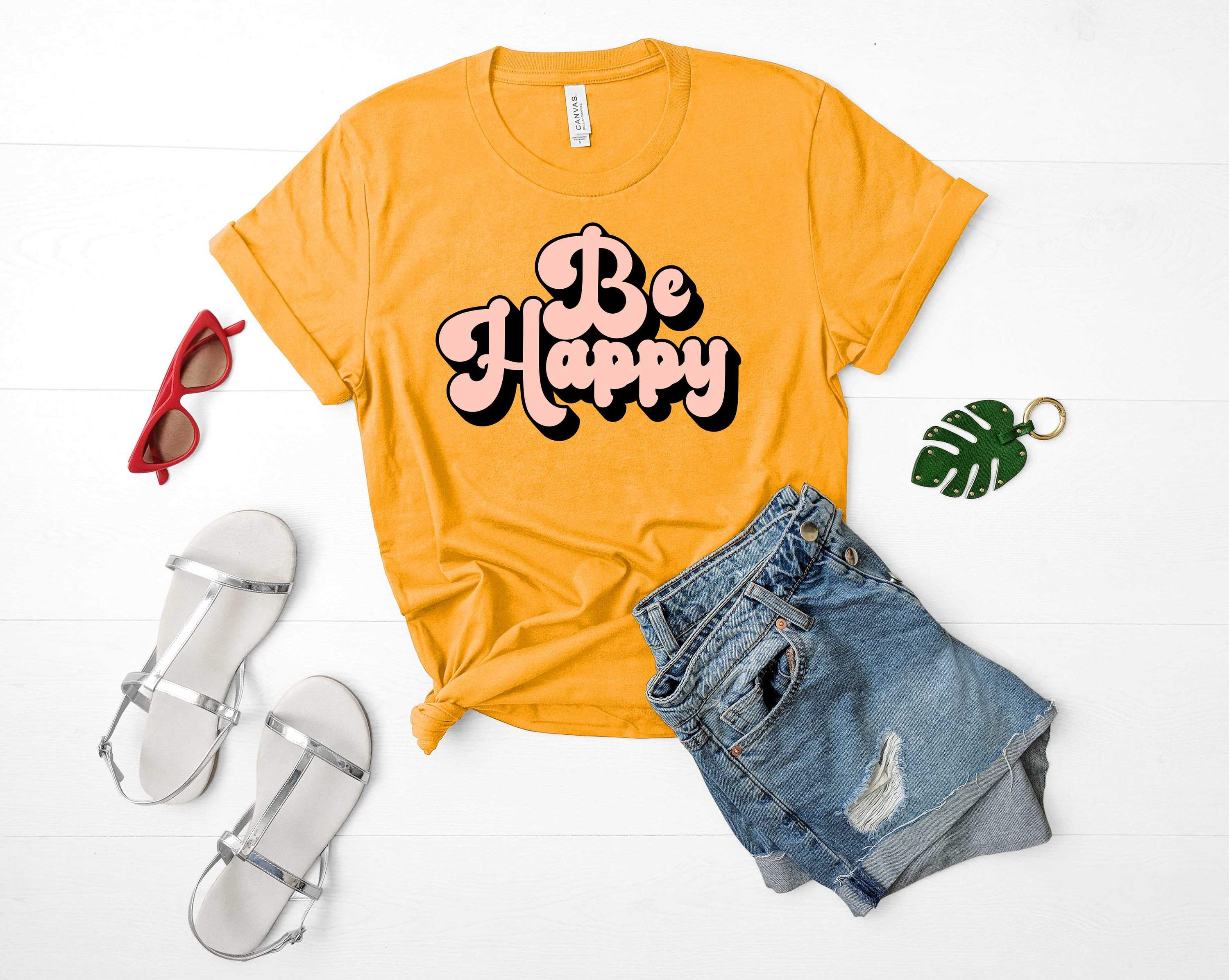 A unisex graphic t-shirt featuring the phrase 'Be Happy' in vibrant colors, perfect for casual wear.