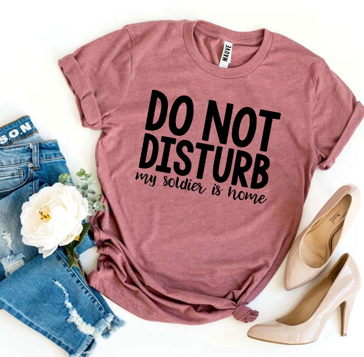 A black T-shirt with the text 'Do Not Disturb My Soldier Is Home' printed in bold letters, showcasing a comfortable and stylish design.