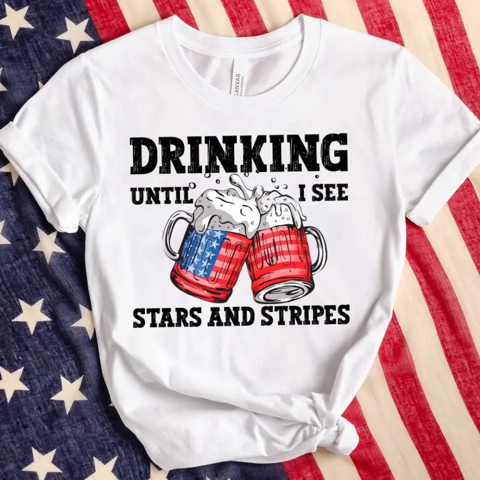 A stylish 4th of July tee featuring the phrase 'Drinking Until I See The Stars And Stripes' in a vibrant design, perfect for summer celebrations.