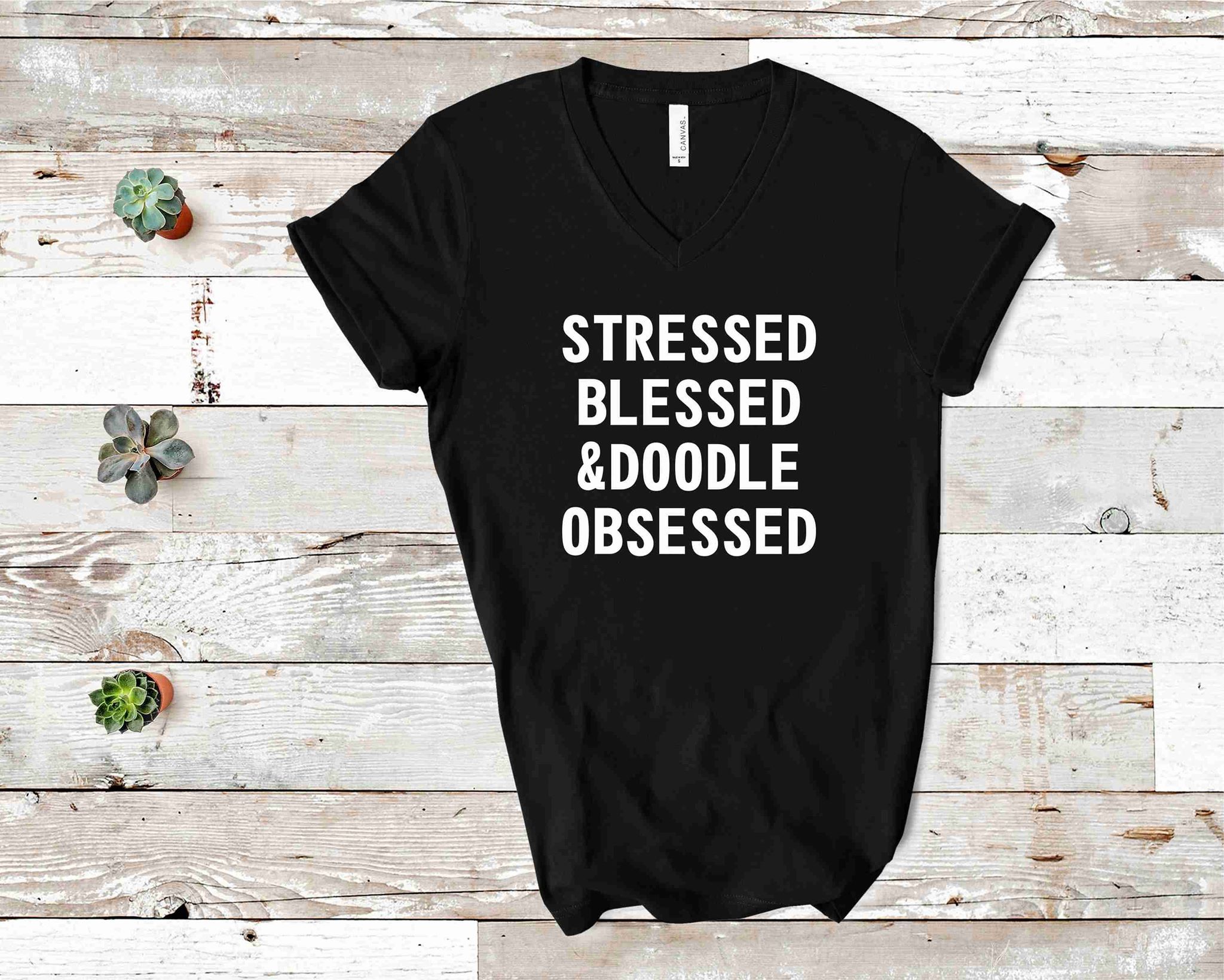 Black graphic t-shirt featuring 'Stressed Blessed Doodle Obsessed' design, short sleeves, and a comfortable fit.