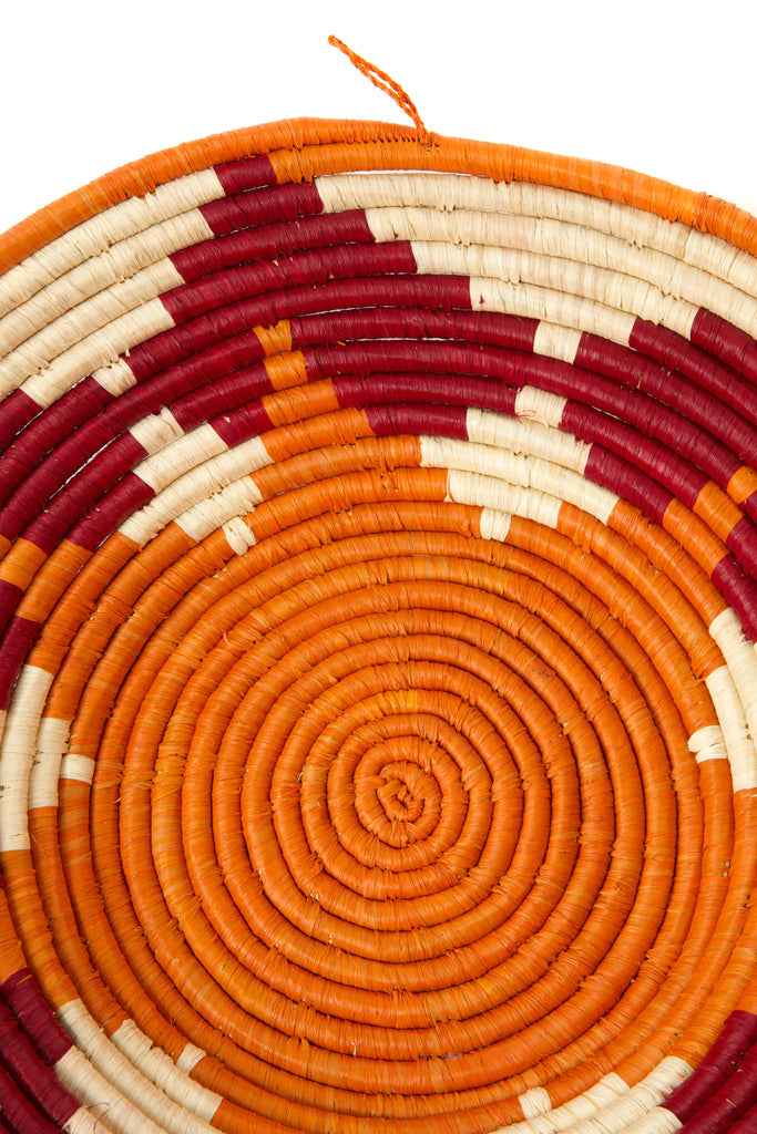 Handwoven sisal coiled African raffia basket in vibrant orange and burgundy, showcasing intricate craftsmanship and natural materials.