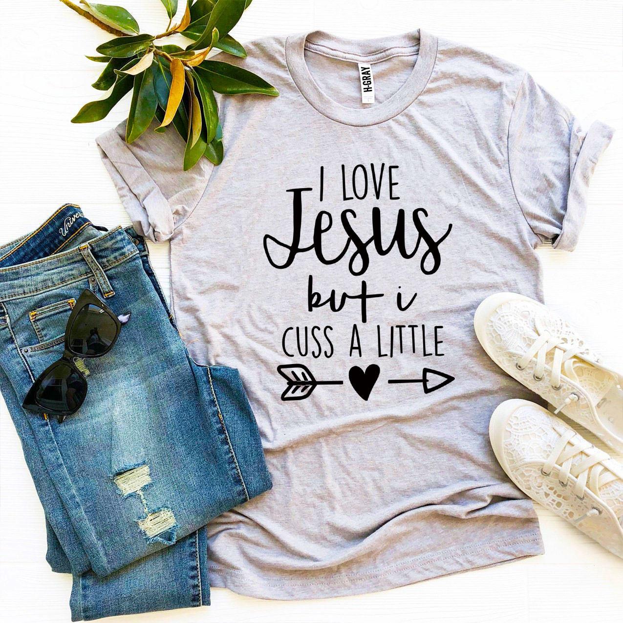 I Love Jesus But I Cuss a Little T-shirt in various sizes, showcasing its soft cotton fabric and humorous design.