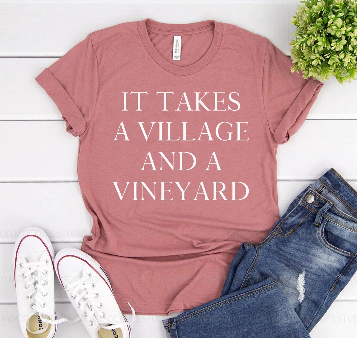 It Takes A Village And A Vineyard T-shirt displayed on a hanger, showcasing its classic unisex design and soft fabric.