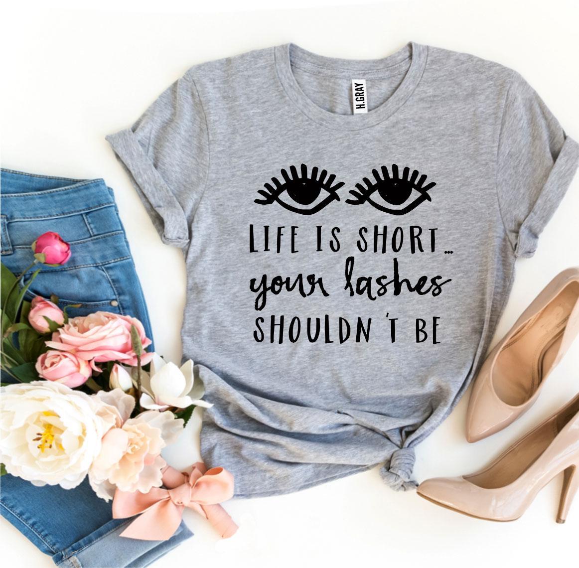 A stylish black t-shirt featuring the phrase 'Life Is Short Your Lashes Shouldn’t Be' in a modern font, made from soft ring spun cotton.