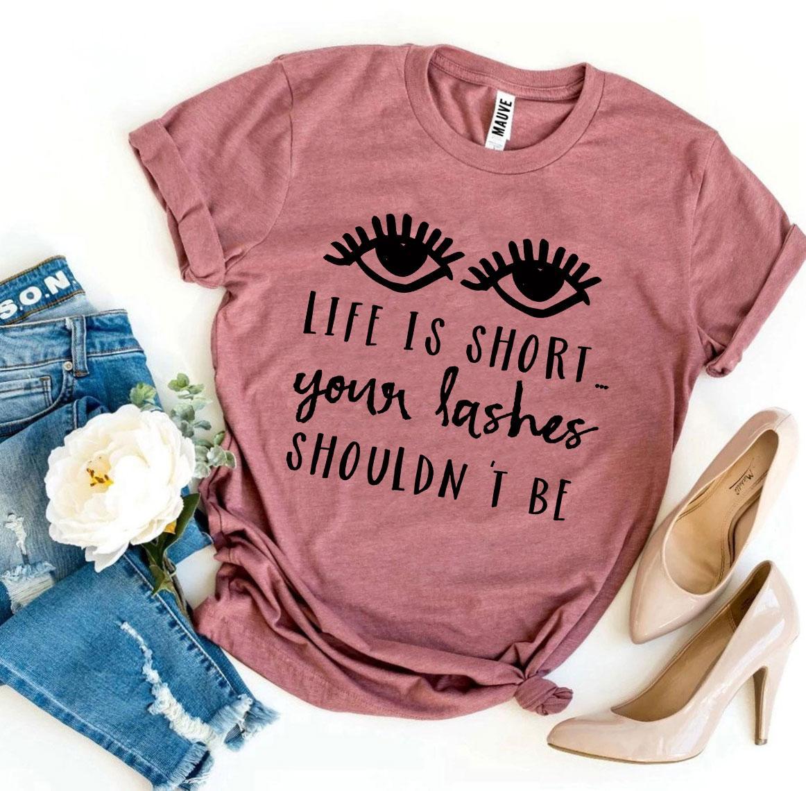 A stylish black t-shirt featuring the phrase 'Life Is Short Your Lashes Shouldn’t Be' in a modern font, made from soft ring spun cotton.