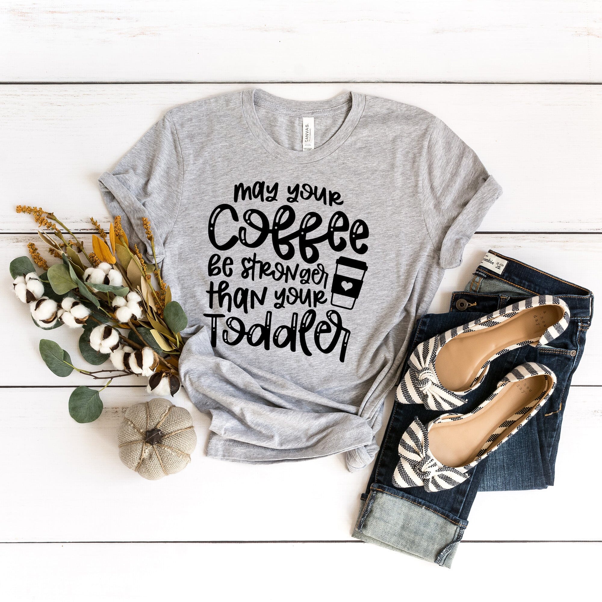 A humorous T-shirt featuring the phrase 'May Your Coffee Be Stronger Than Your Toddler', made from soft cotton, suitable for both men and women.