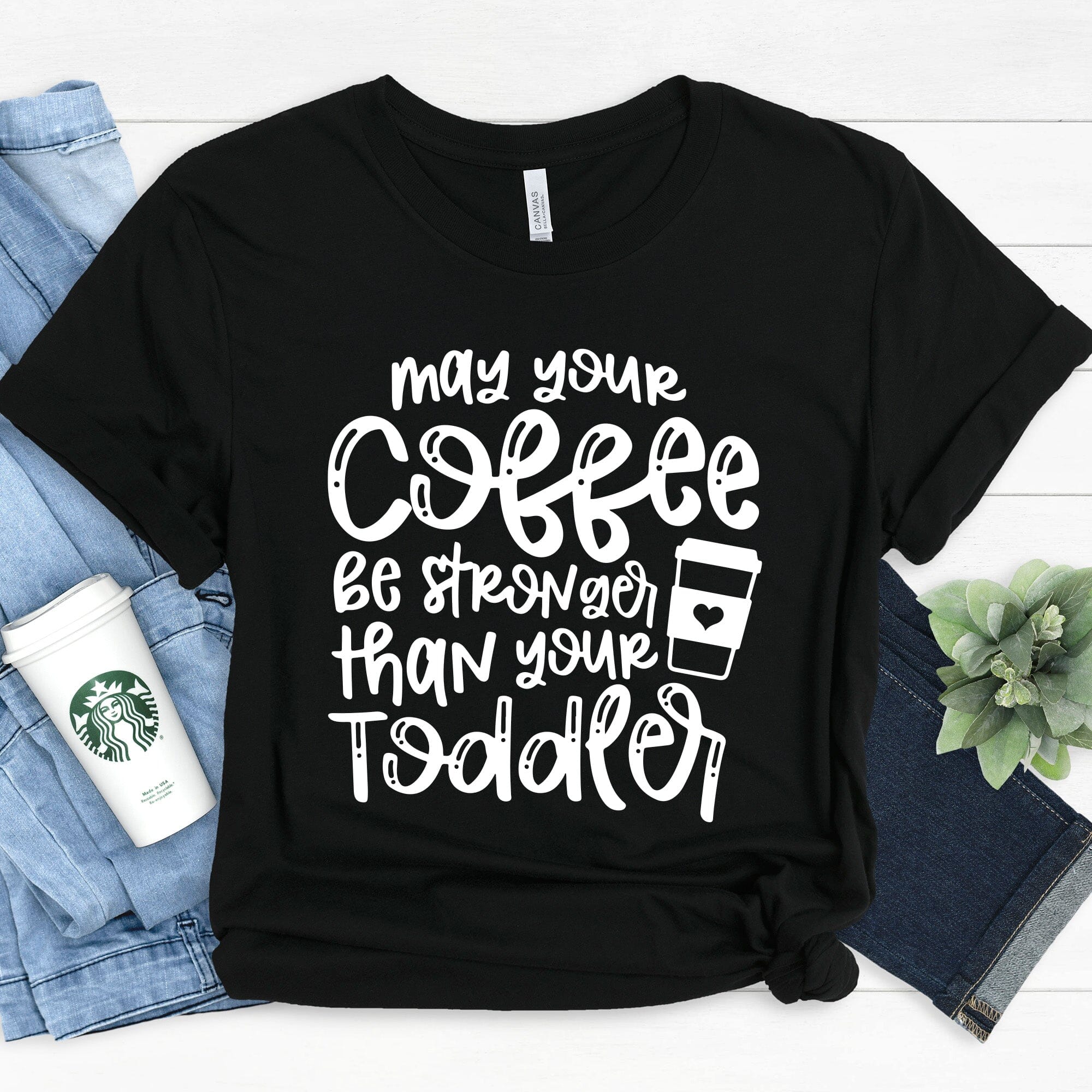 A humorous T-shirt featuring the phrase 'May Your Coffee Be Stronger Than Your Toddler', made from soft cotton, suitable for both men and women.