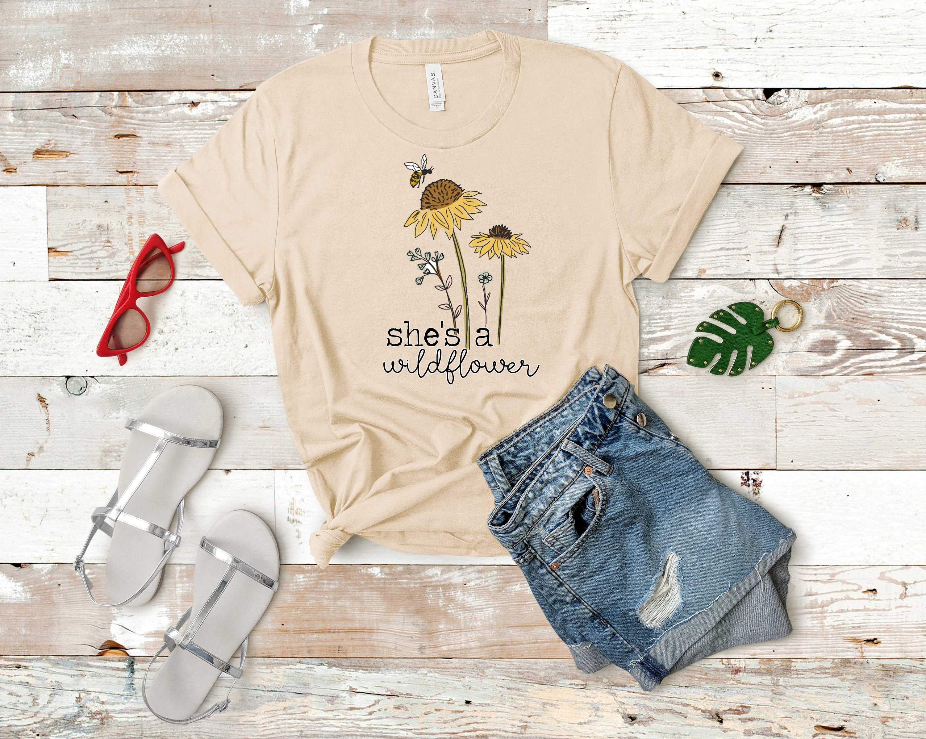 A unisex graphic tee featuring the phrase 'She's a Wildflower' in a stylish design, perfect for casual wear.