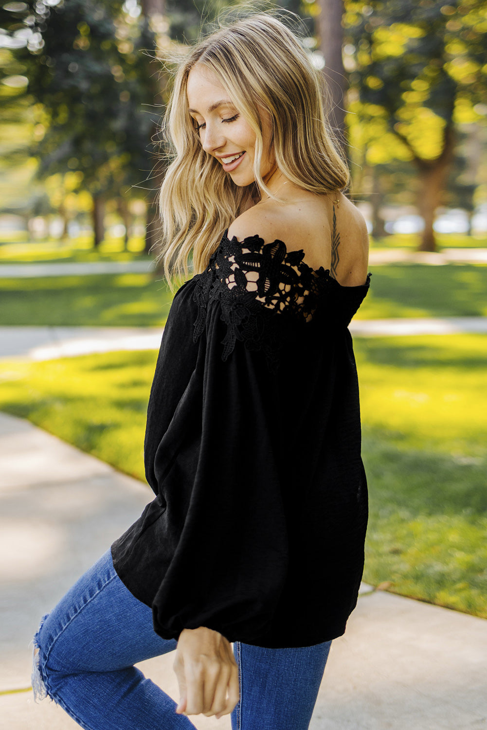 A stylish woman wearing a Blooming Lace Off The Shoulder Top, showcasing its elegant design and lace detailing.