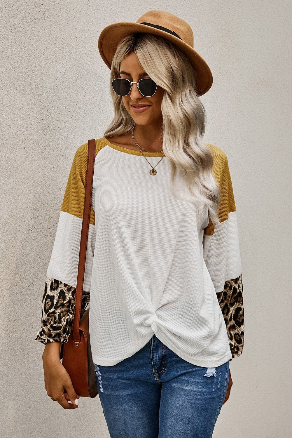 A stylish Knit White Blouse featuring long sleeves, leopard print cuffs, and a relaxed fit with a twisted front tie hem.