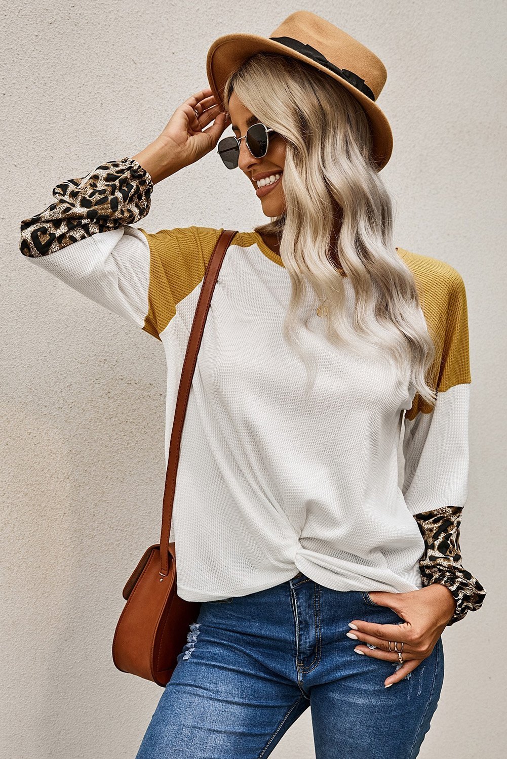 A stylish Knit White Blouse featuring long sleeves, leopard print cuffs, and a relaxed fit with a twisted front tie hem.