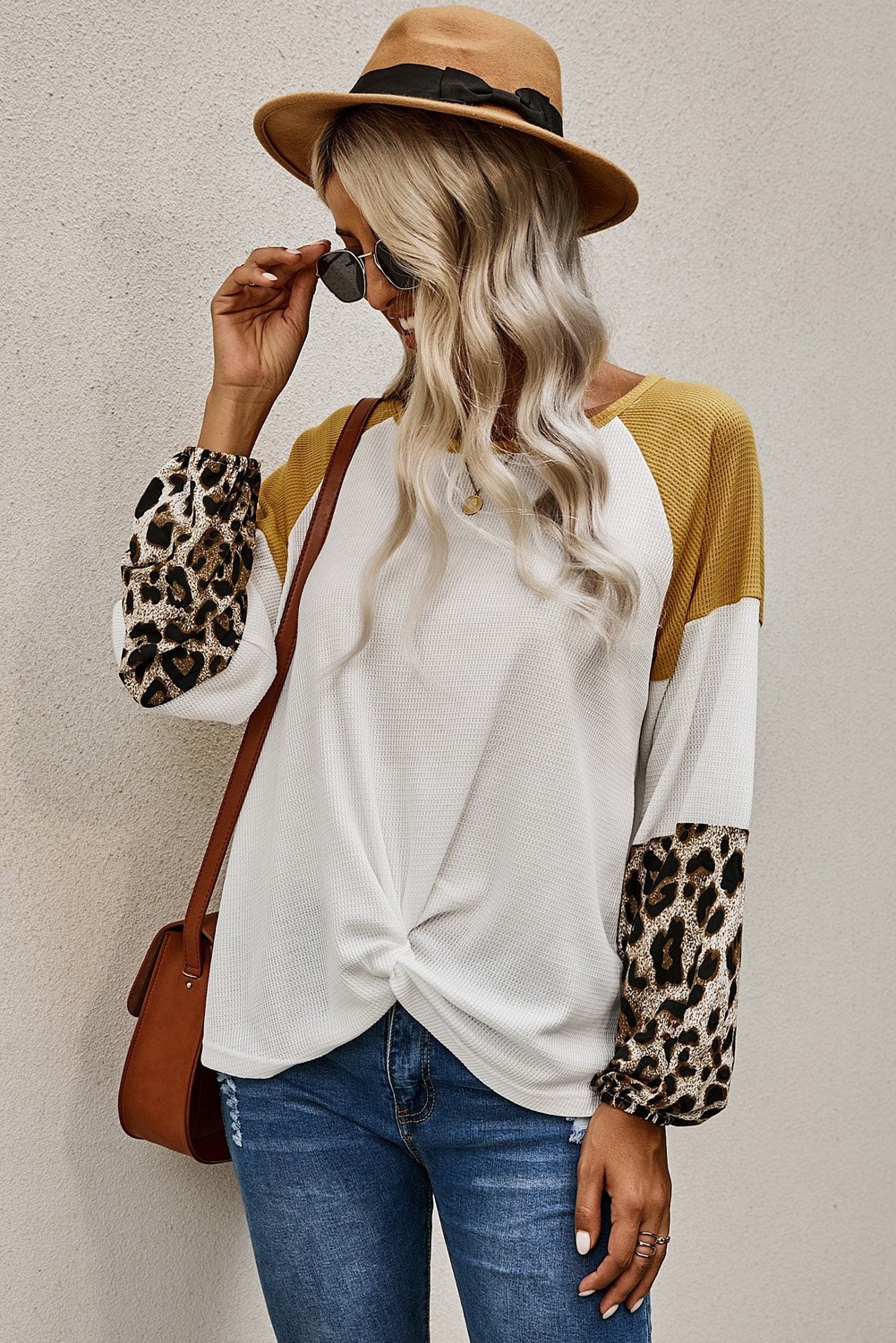 A stylish Knit White Blouse featuring long sleeves, leopard print cuffs, and a relaxed fit with a twisted front tie hem.