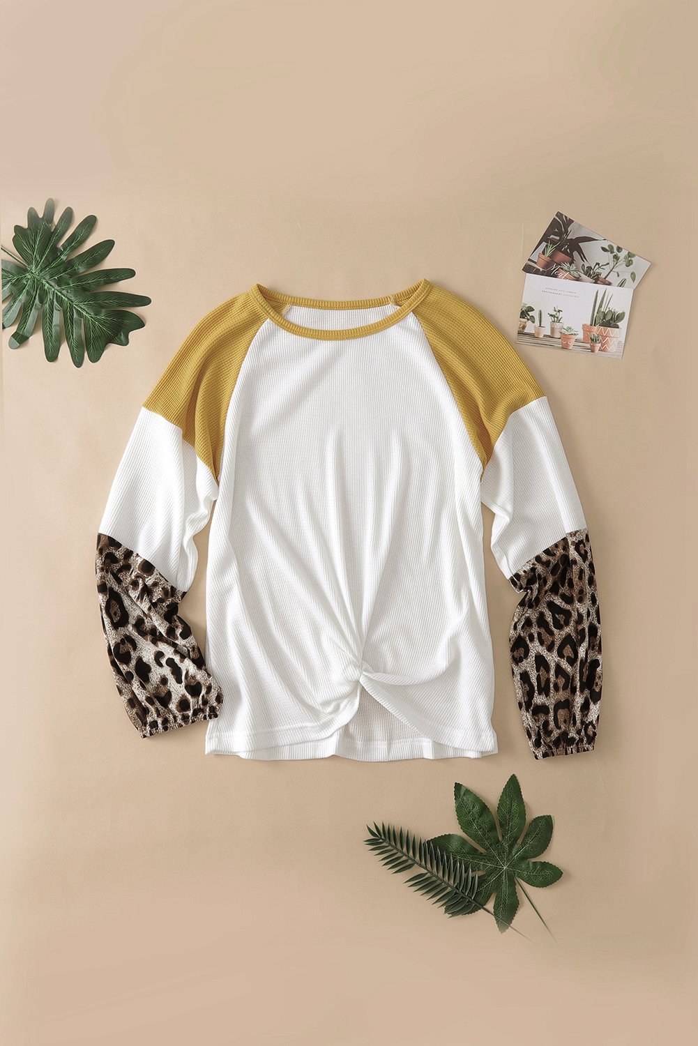 A stylish Knit White Blouse featuring long sleeves, leopard print cuffs, and a relaxed fit with a twisted front tie hem.