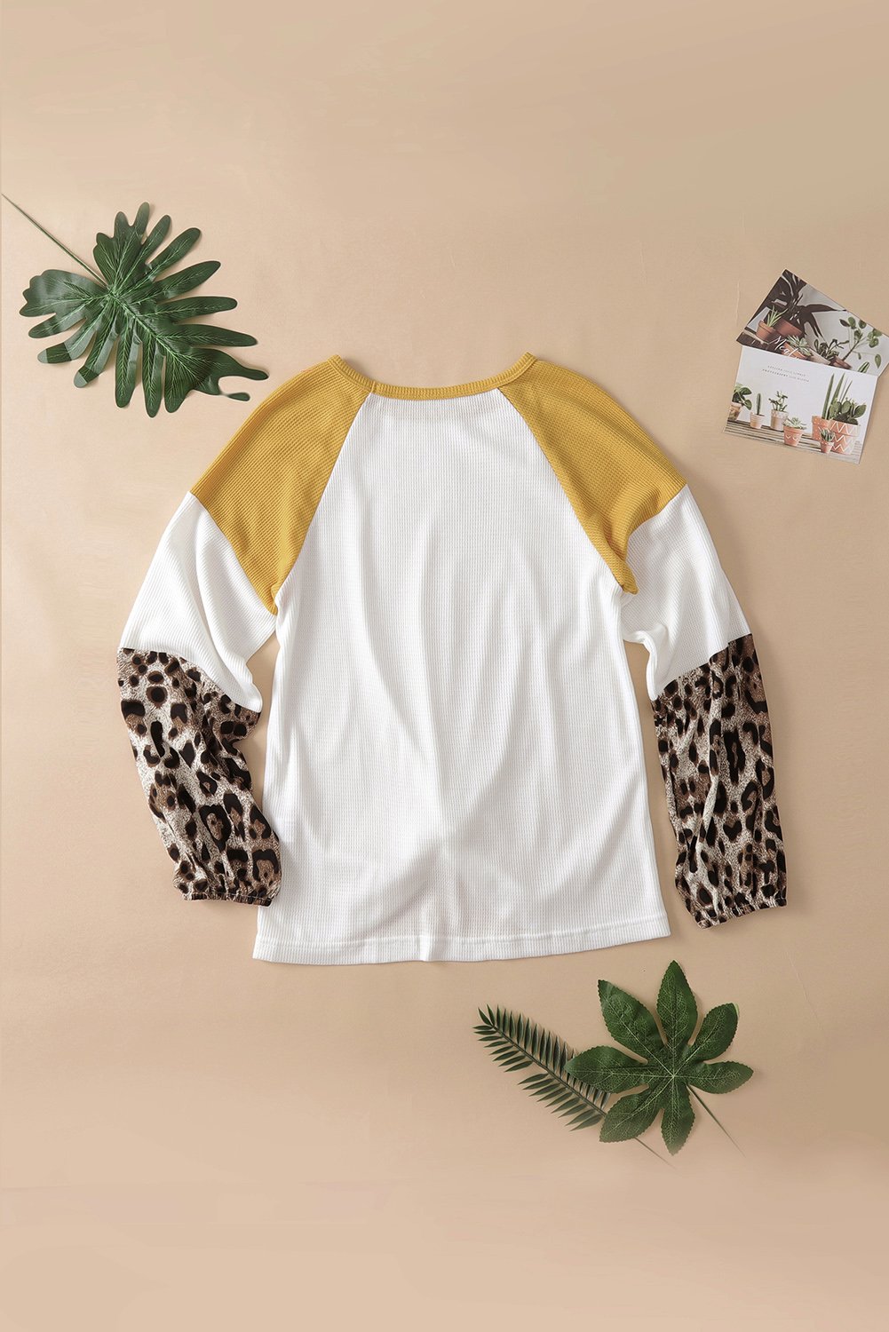 A stylish Knit White Blouse featuring long sleeves, leopard print cuffs, and a relaxed fit with a twisted front tie hem.