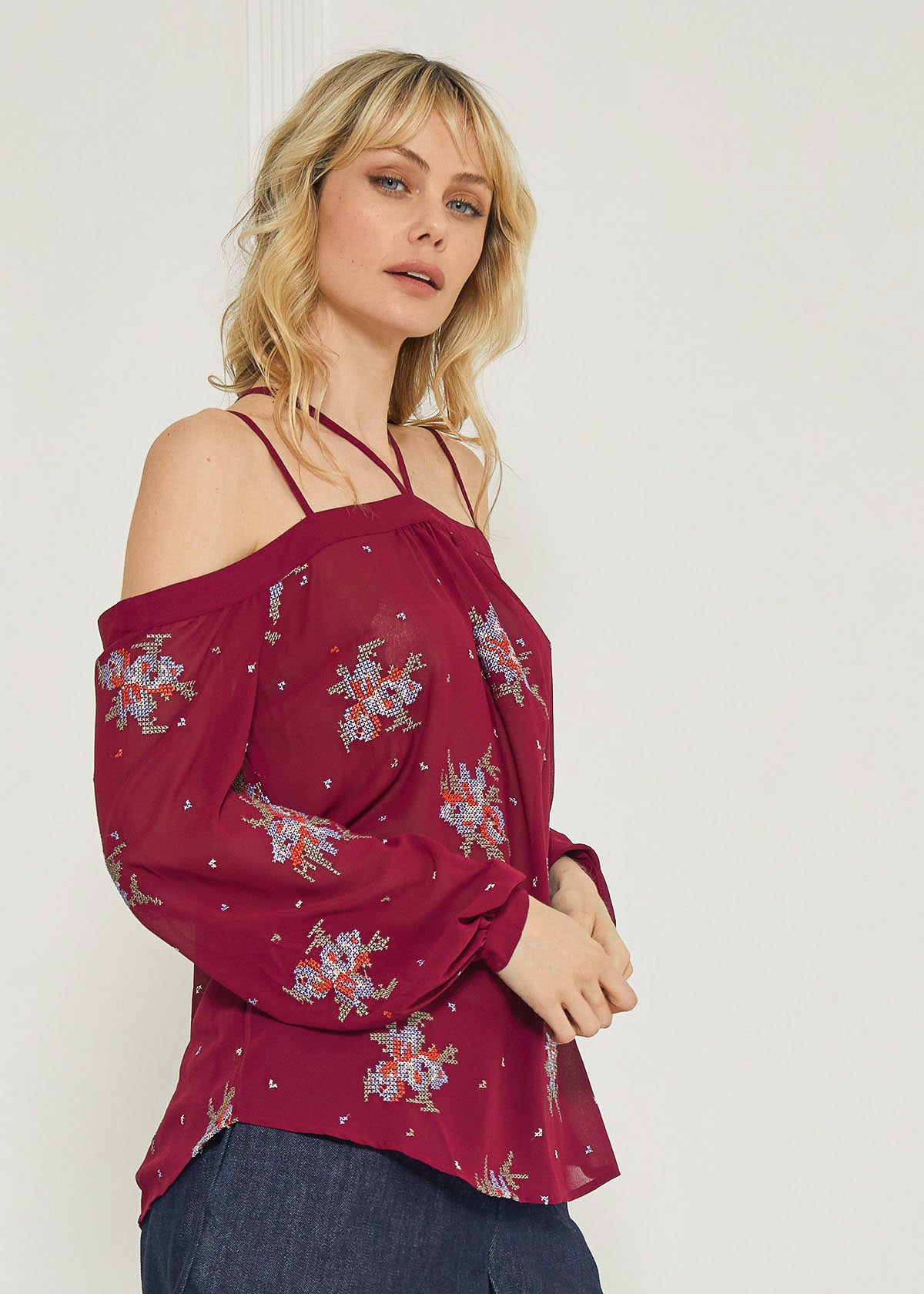 A stylish off-shoulder blouse in burgundy featuring intricate embroidery prints, perfect for dressing up denim outfits.