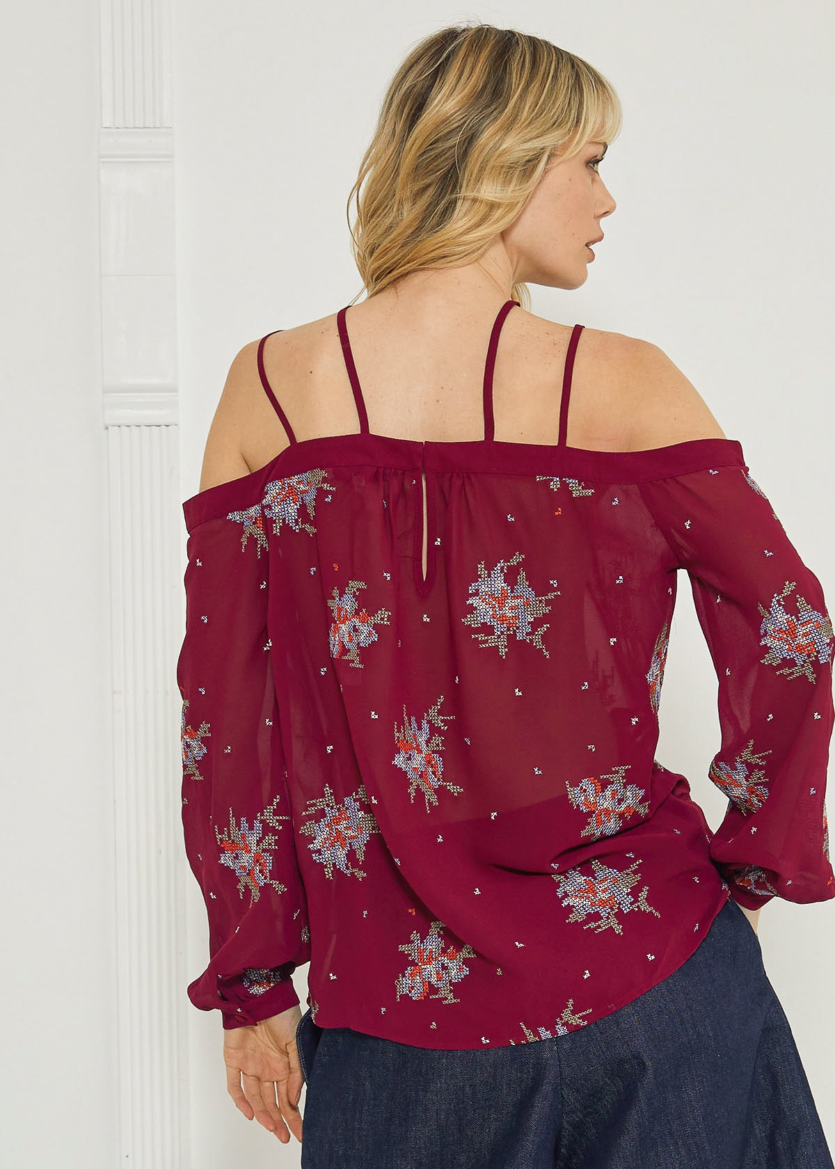 A stylish off-shoulder blouse in burgundy featuring intricate embroidery prints, perfect for dressing up denim outfits.